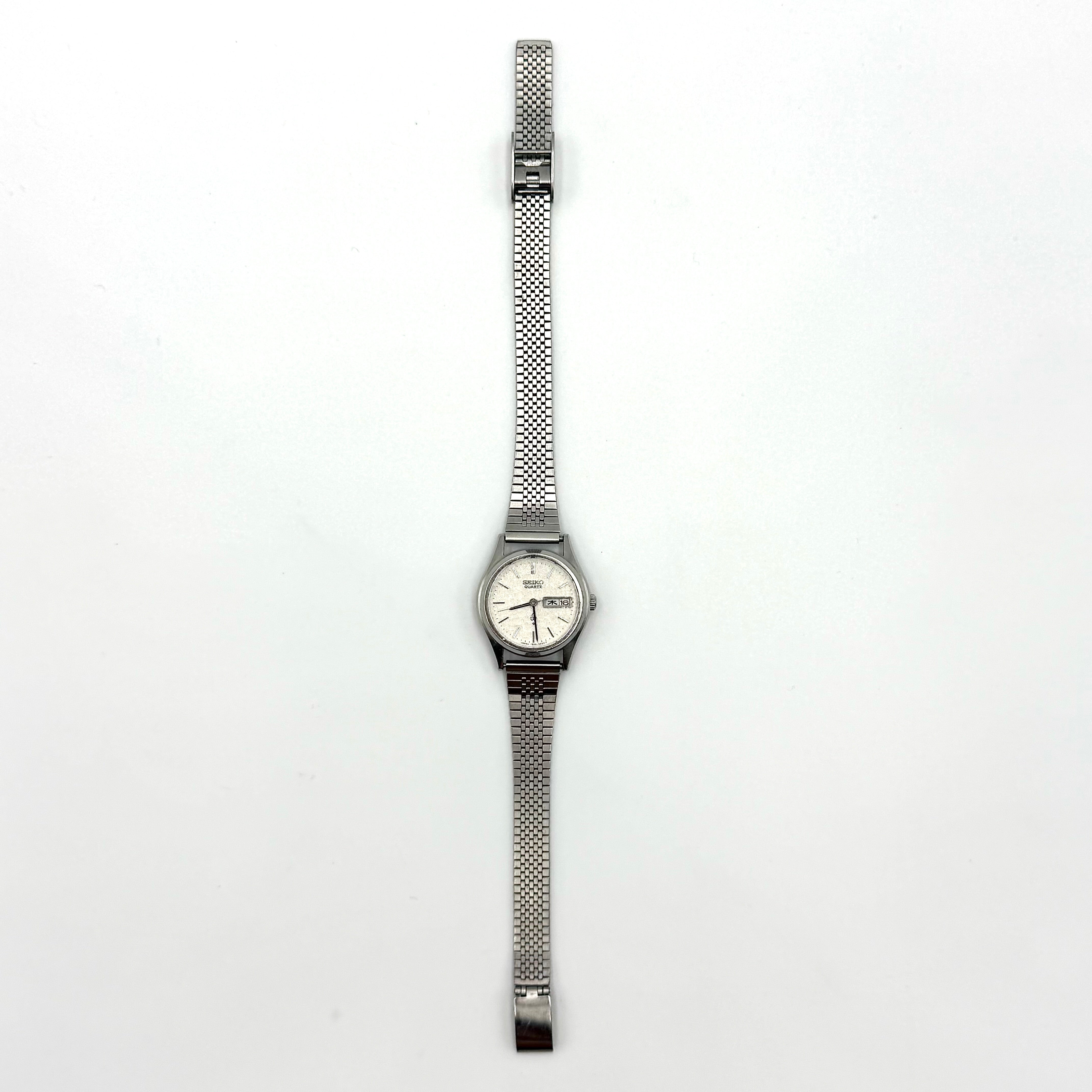 Seiko 7903-0030 Quartz stainless steel watch with a white textured dial and matching steel bracelet on a display pillow.