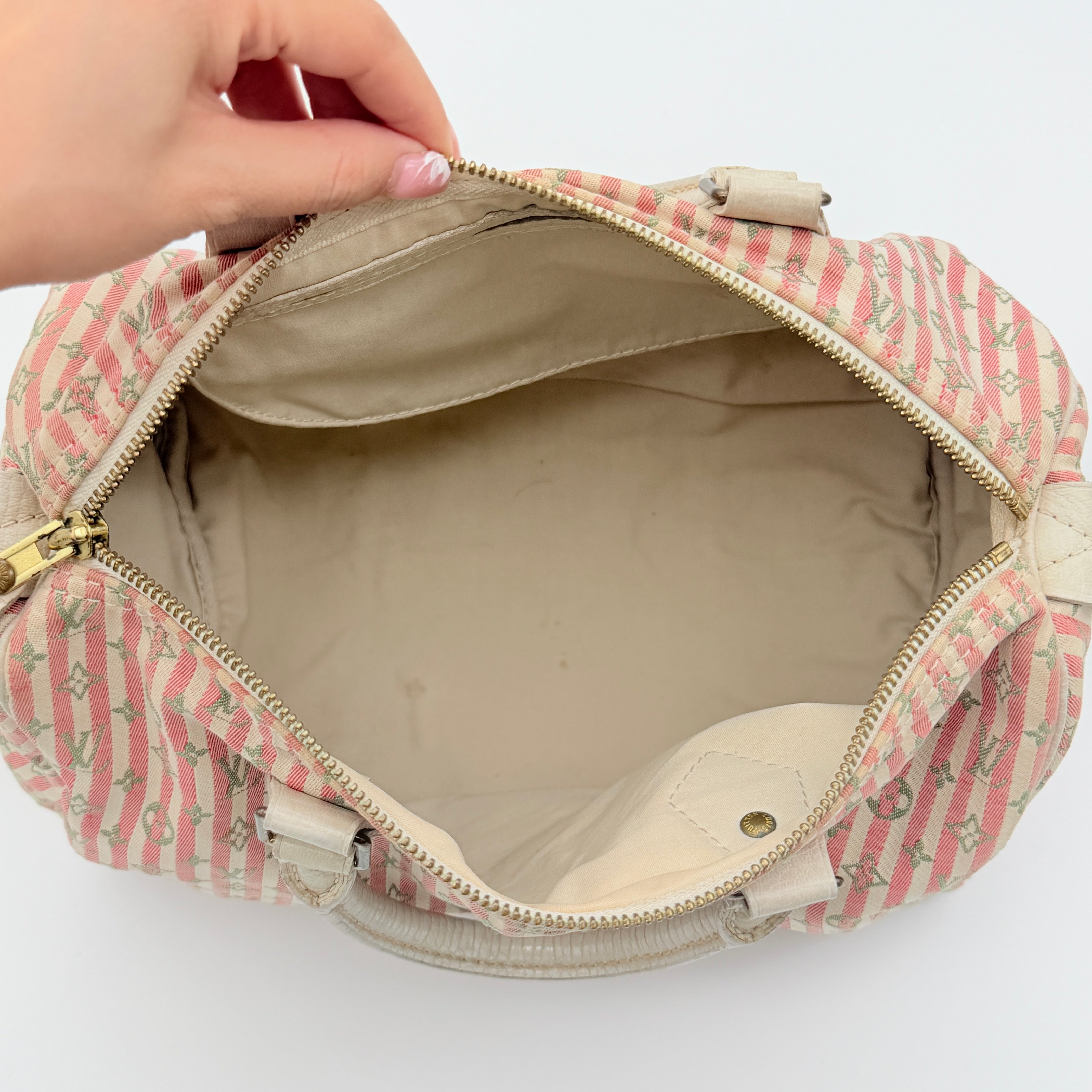 Louis Vuitton Speedy 30 in pink Mini Lin Monogram with cream leather handles and gold-tone zip, displayed on a neutral background.
