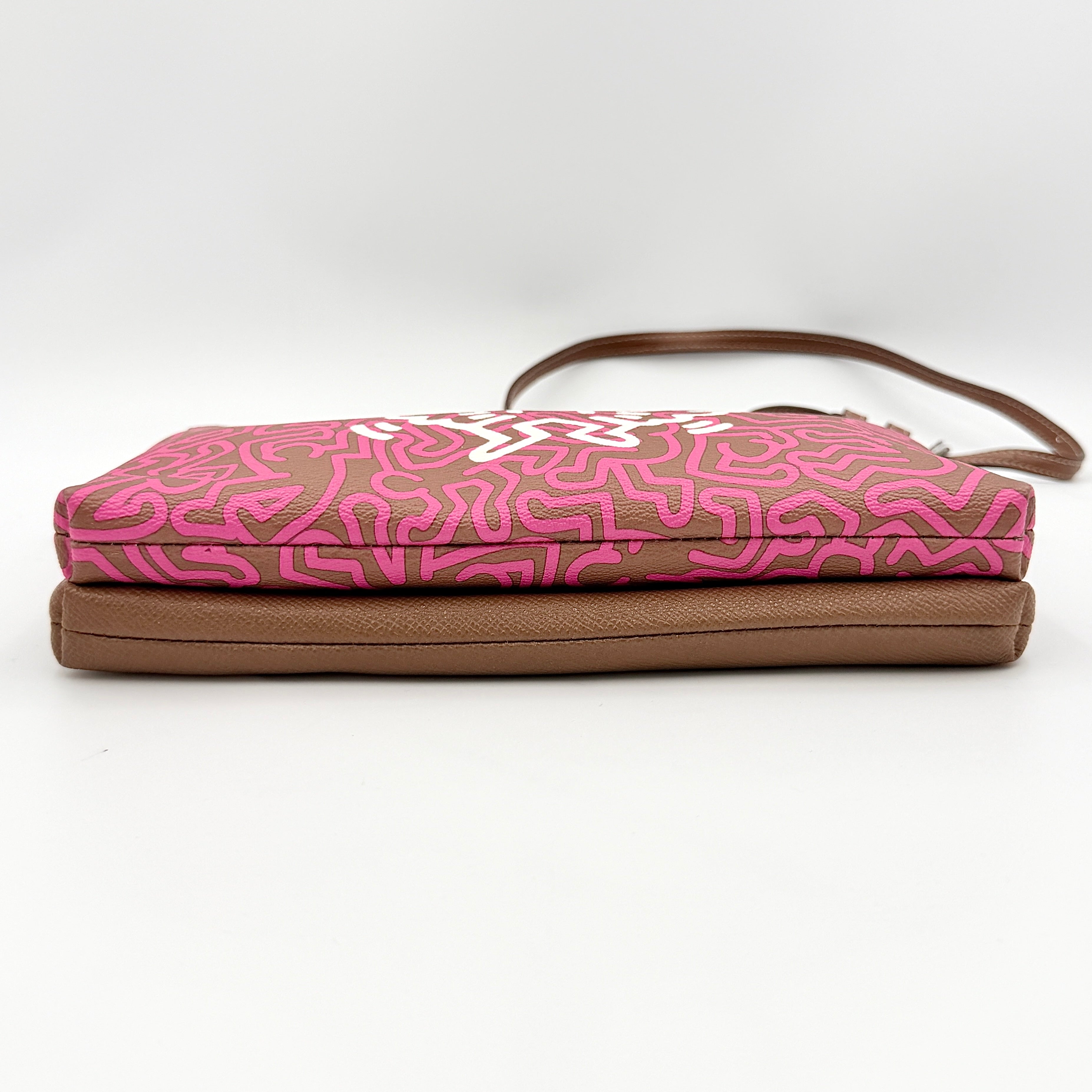 Coach x Keith Haring Lyla Crossbody bag in textured brown leather with bold pink graphic pattern and white artwork, featuring an adjustable strap.