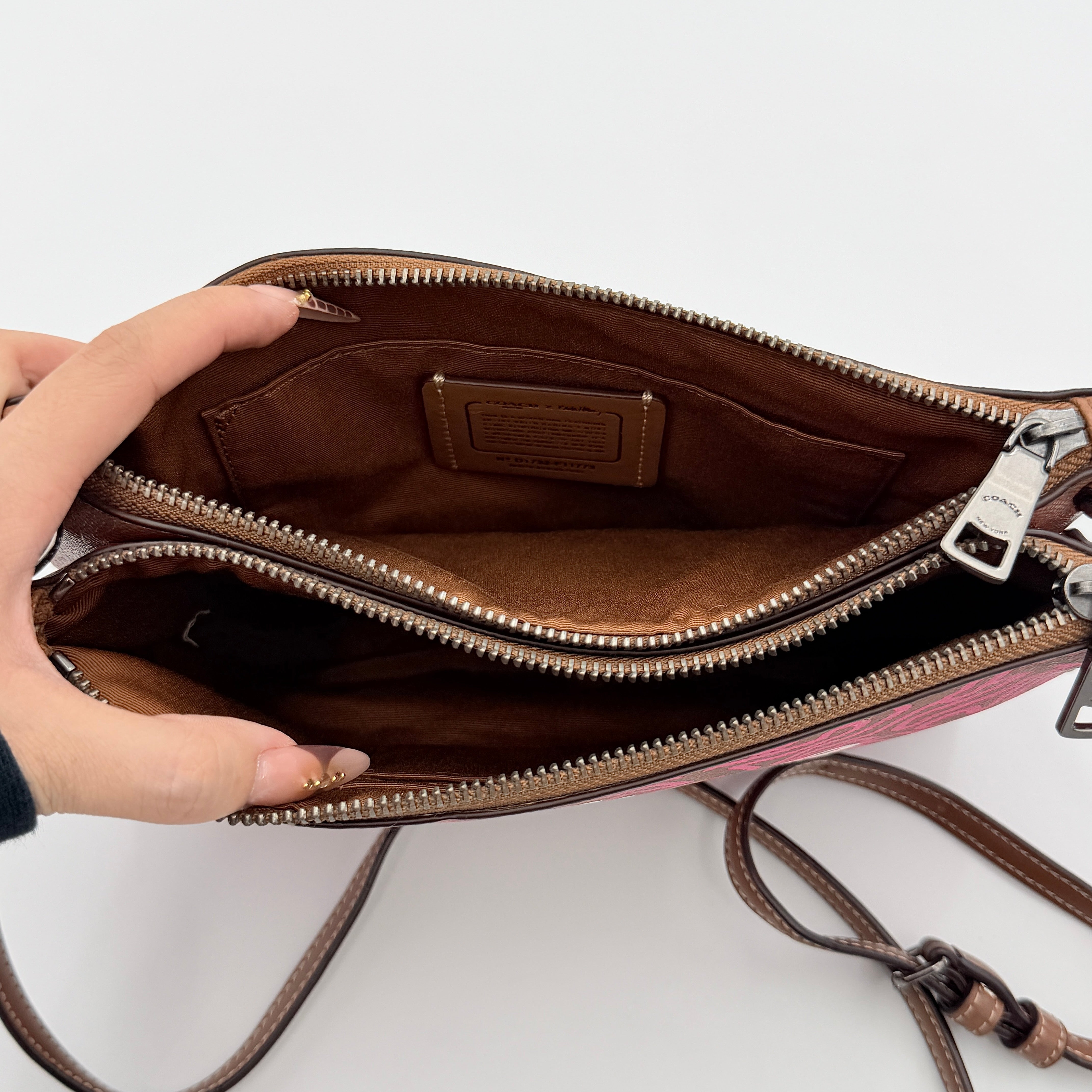Coach x Keith Haring Lyla Crossbody bag in textured brown leather with bold pink graphic pattern and white artwork, featuring an adjustable strap.