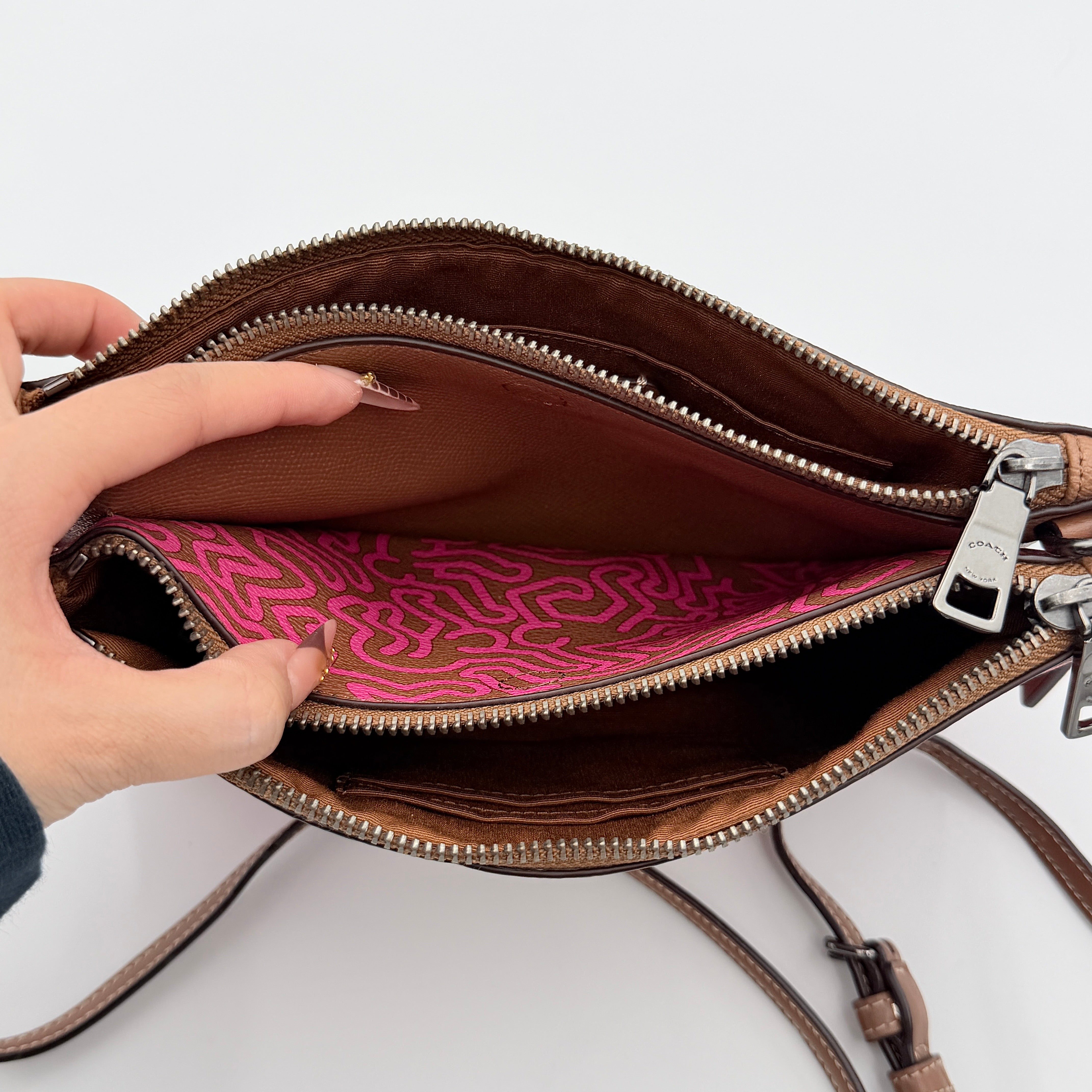 Coach x Keith Haring Lyla Crossbody bag in textured brown leather with bold pink graphic pattern and white artwork, featuring an adjustable strap.