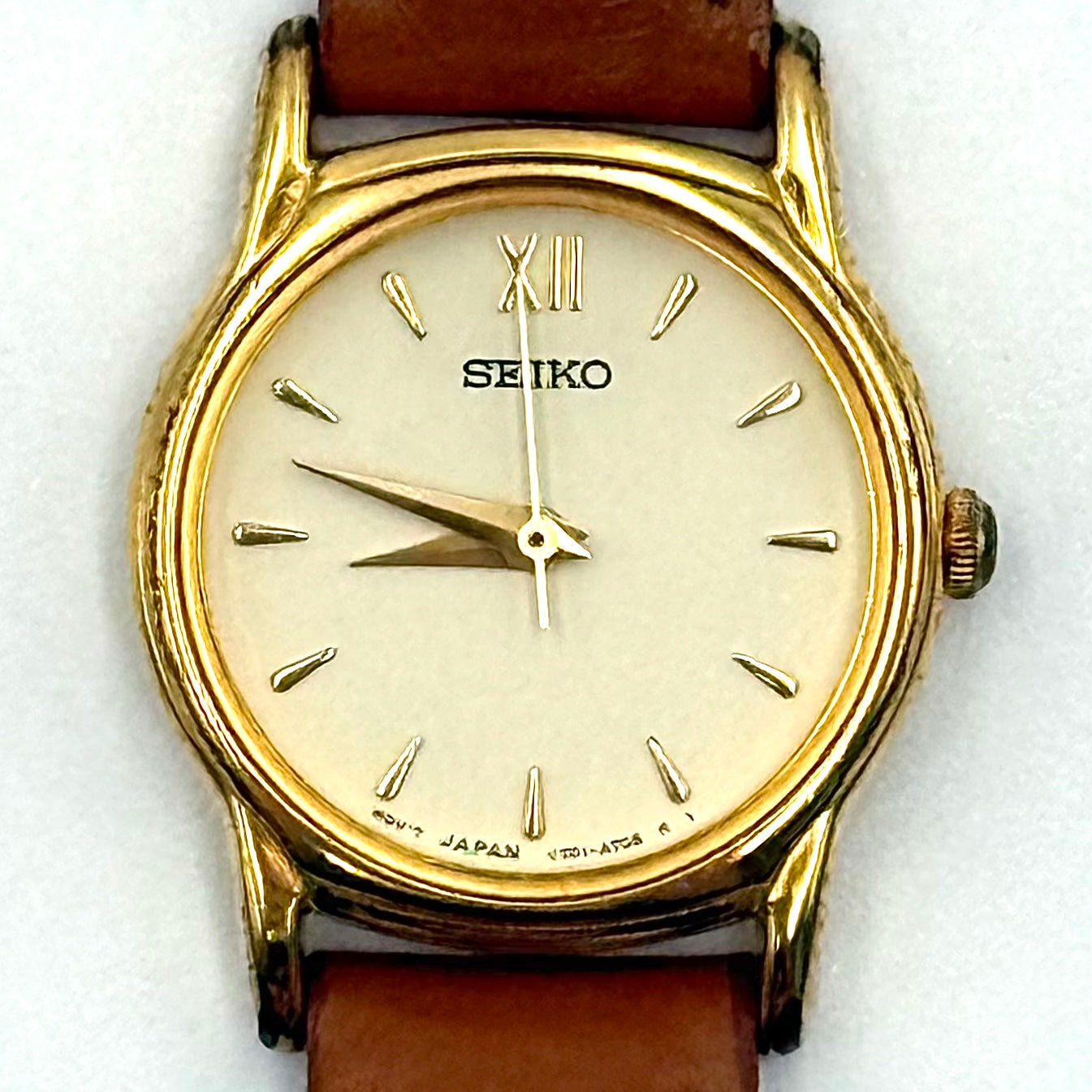 Seiko V701-A110 quartz watch with gold-tone case, cream dial, and brown leather strap on a display pillow.