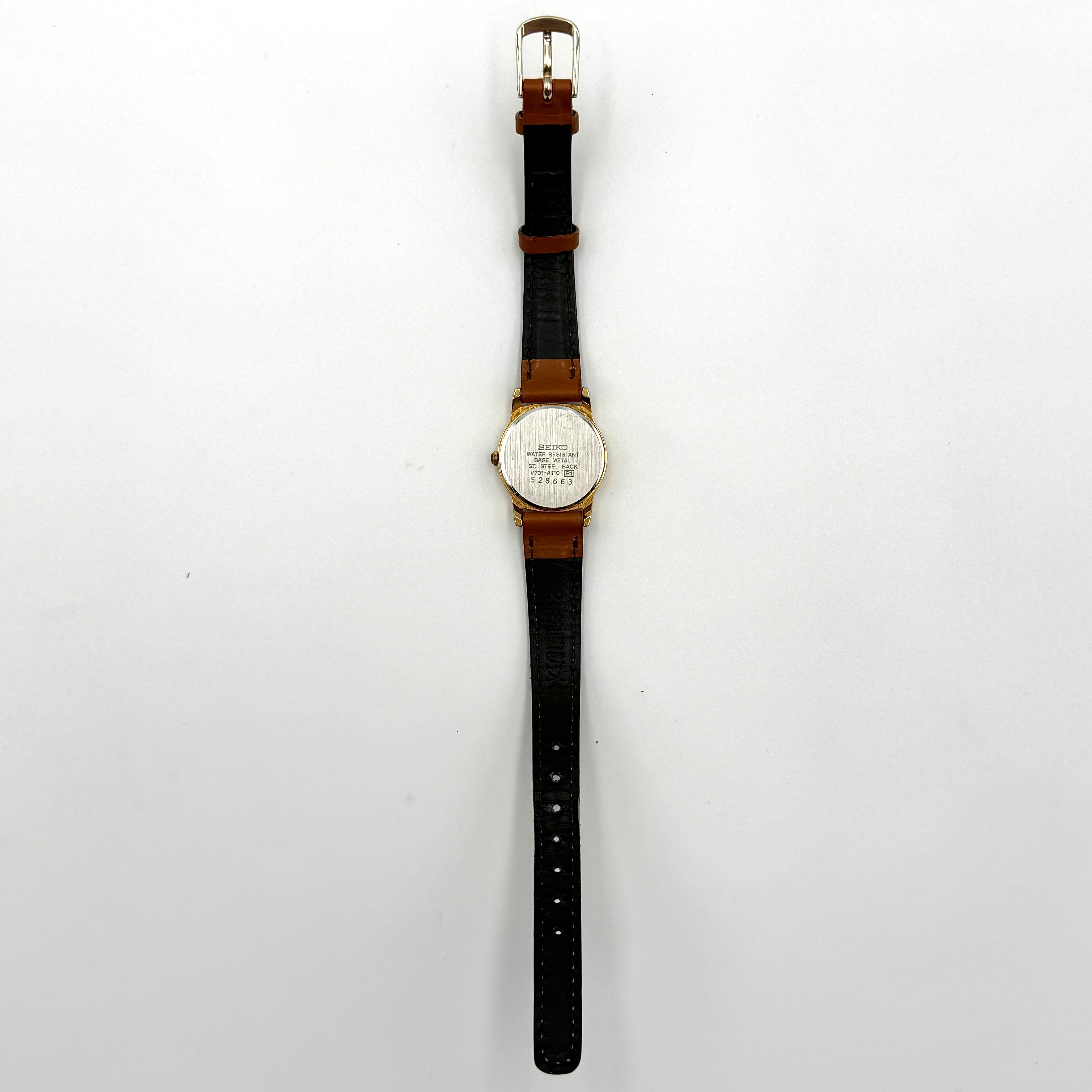 Seiko V701-A110 quartz watch with gold-tone case, cream dial, and brown leather strap on a display pillow.