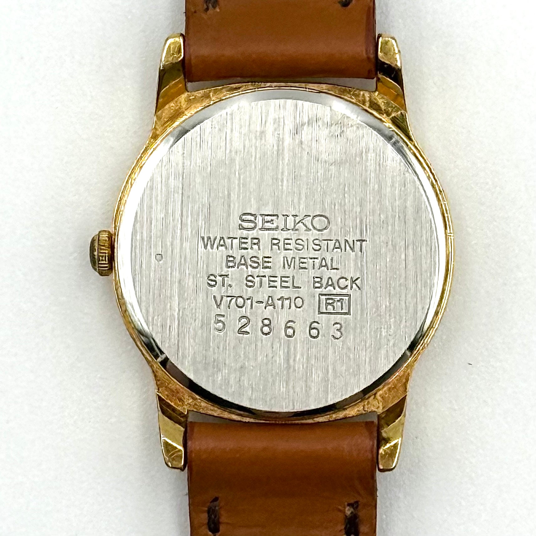 Seiko V701-A110 quartz watch with gold-tone case, cream dial, and brown leather strap on a display pillow.