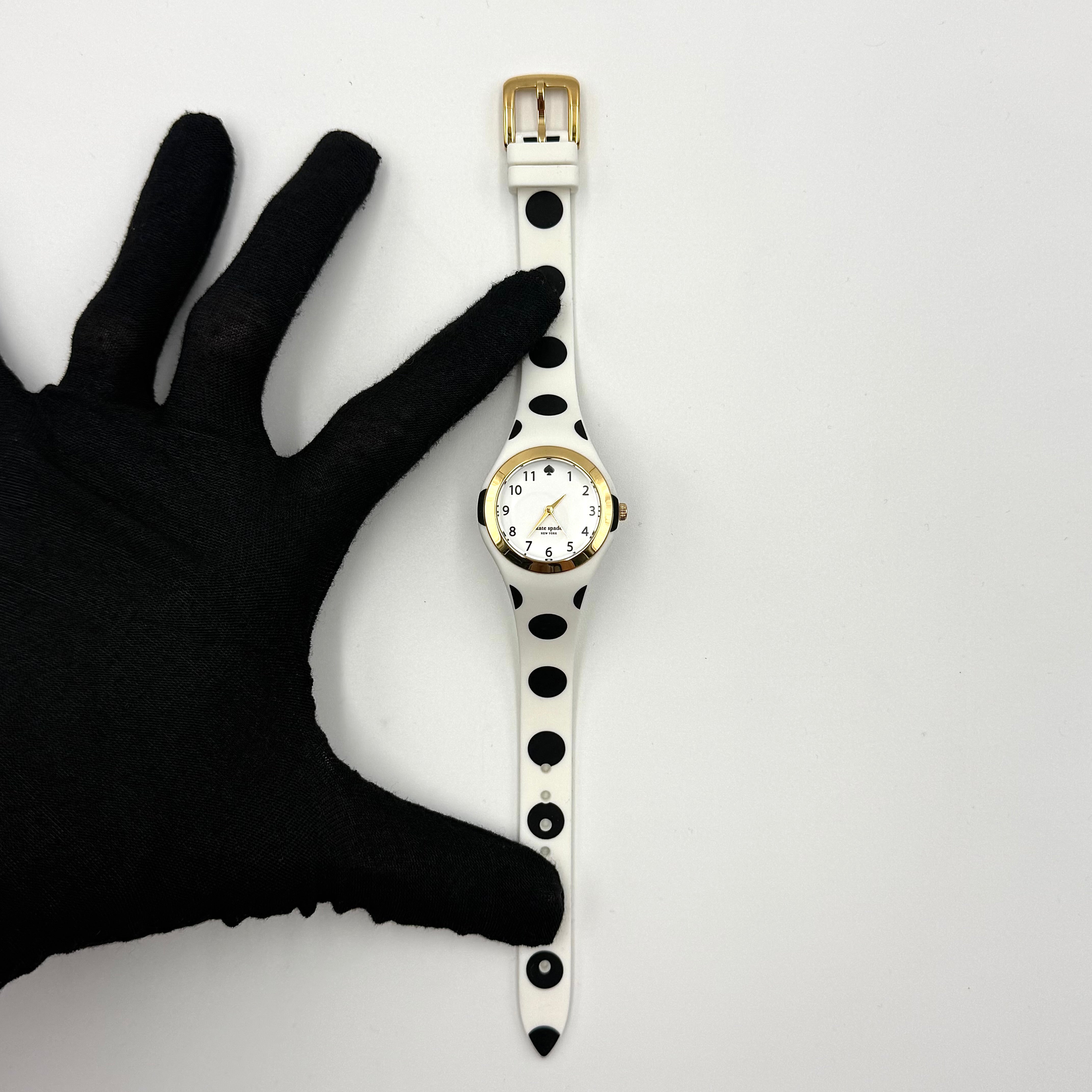 Kate Spade New York Rumsey 0838 silicone watch in white with black polka dots, gold-tone bezel, and white dial displayed on a cushion.