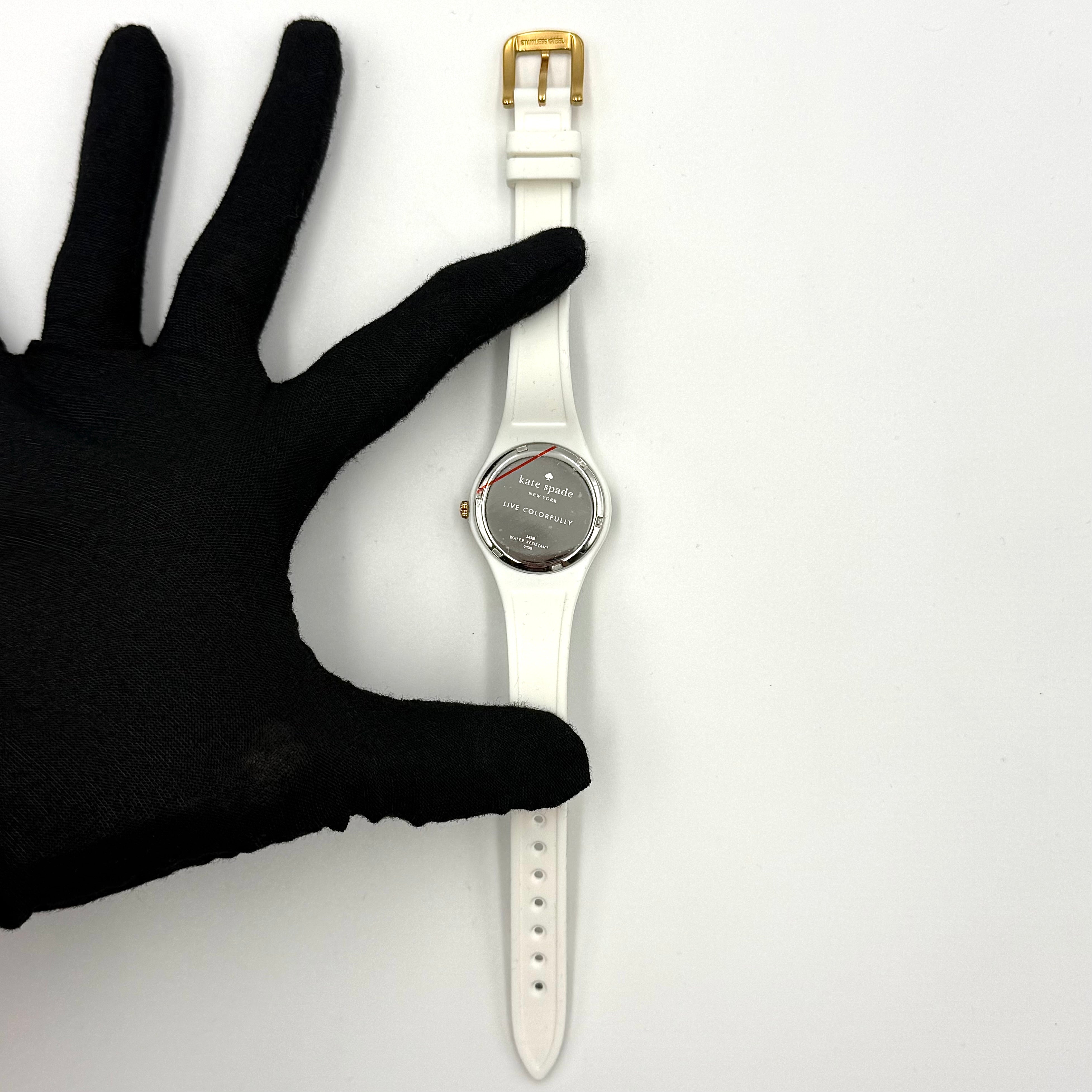 Kate Spade New York Rumsey 0838 silicone watch in white with black polka dots, gold-tone bezel, and white dial displayed on a cushion.
