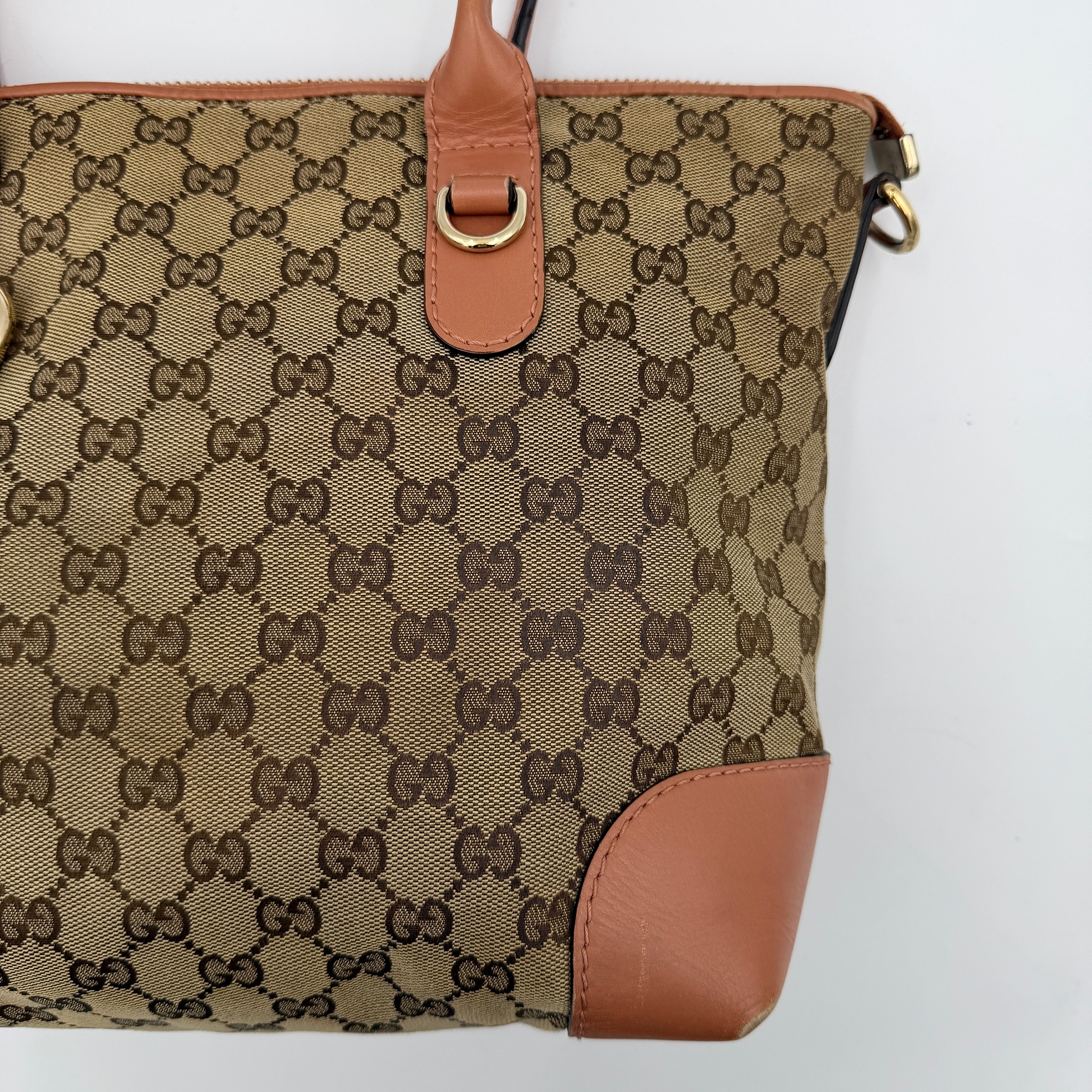 Gucci beige GG monogram shoulder bag with orange leather trim, heart bit charm, and detachable strap displayed on a white background.