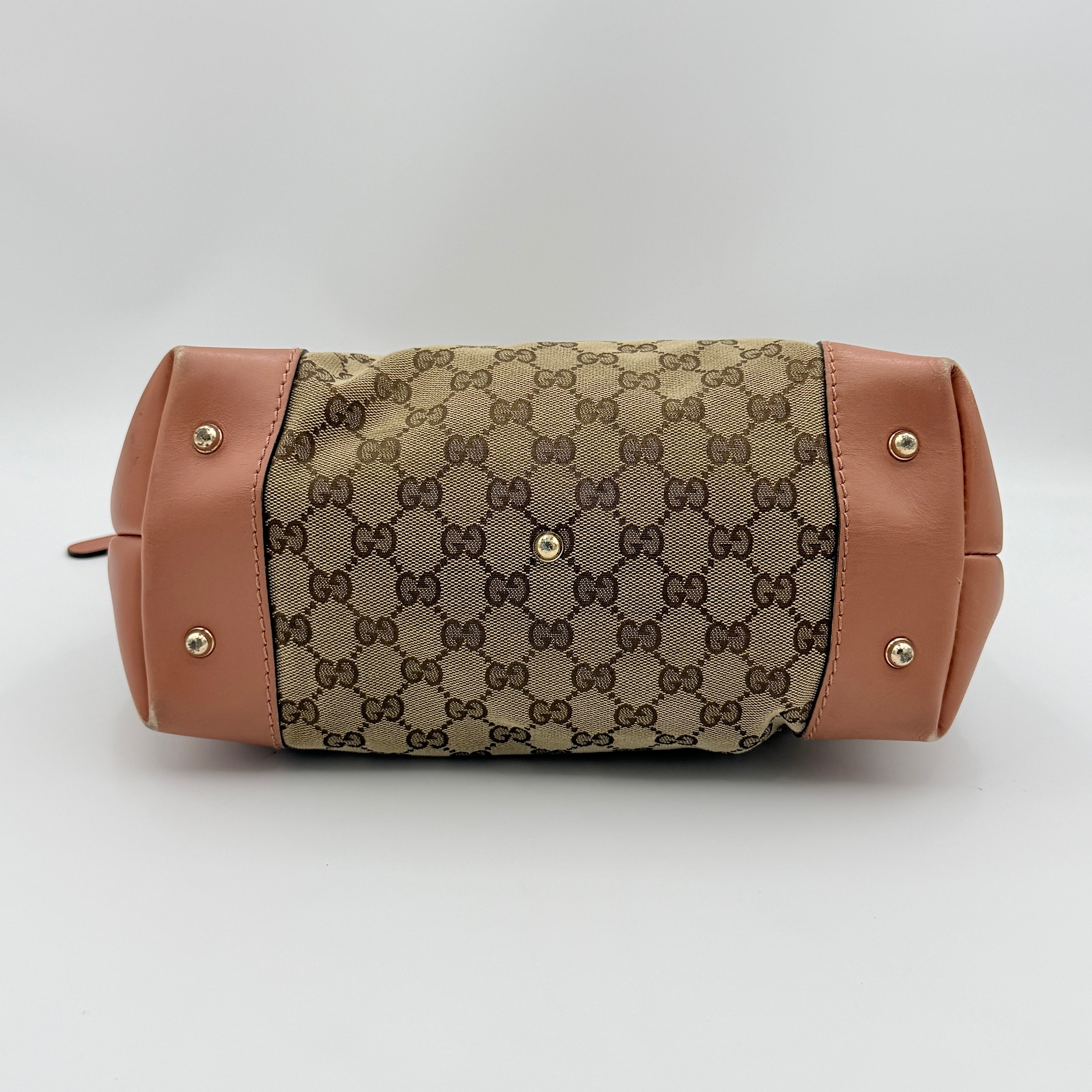 Gucci beige GG monogram shoulder bag with orange leather trim, heart bit charm, and detachable strap displayed on a white background.