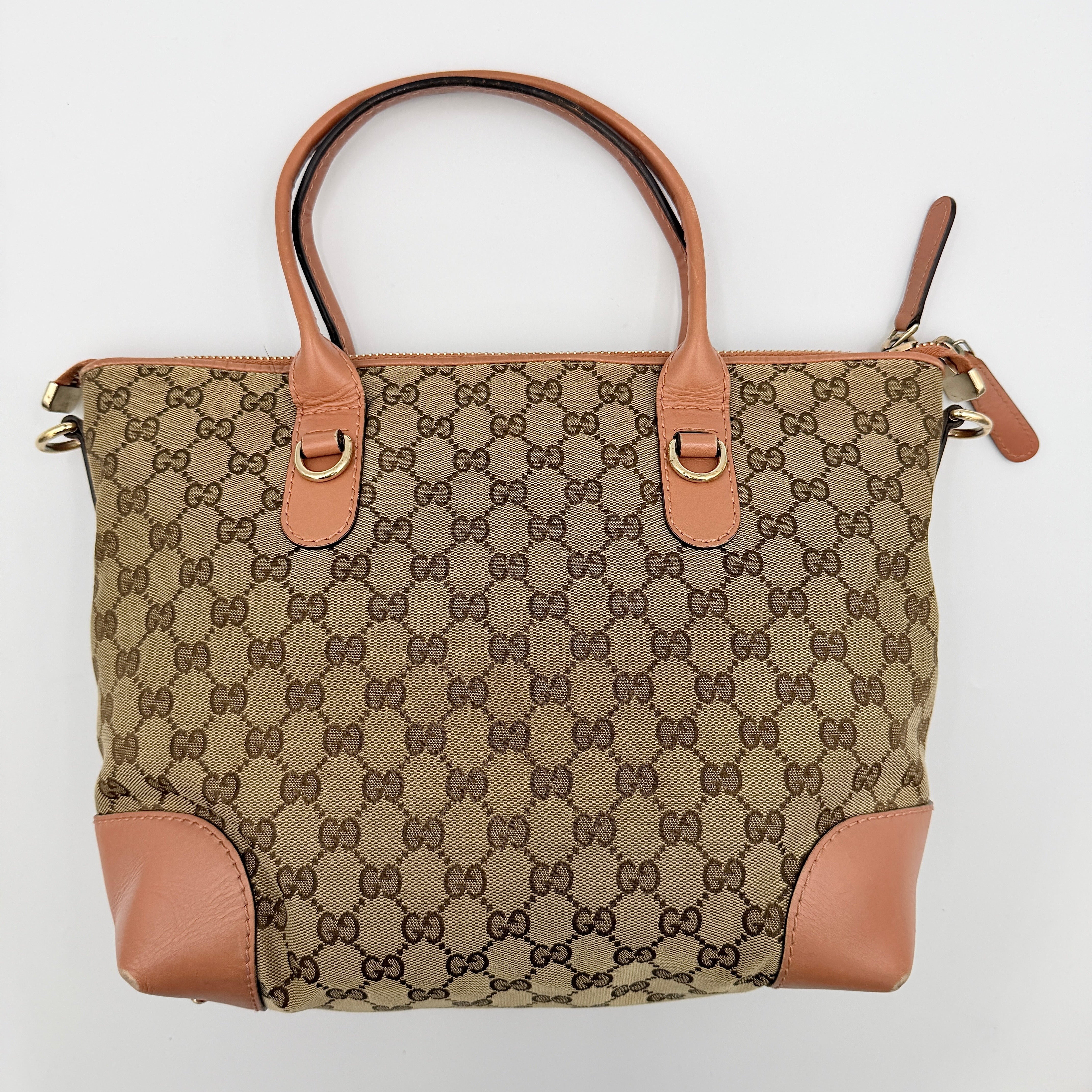 Gucci beige GG monogram shoulder bag with orange leather trim, heart bit charm, and detachable strap displayed on a white background.