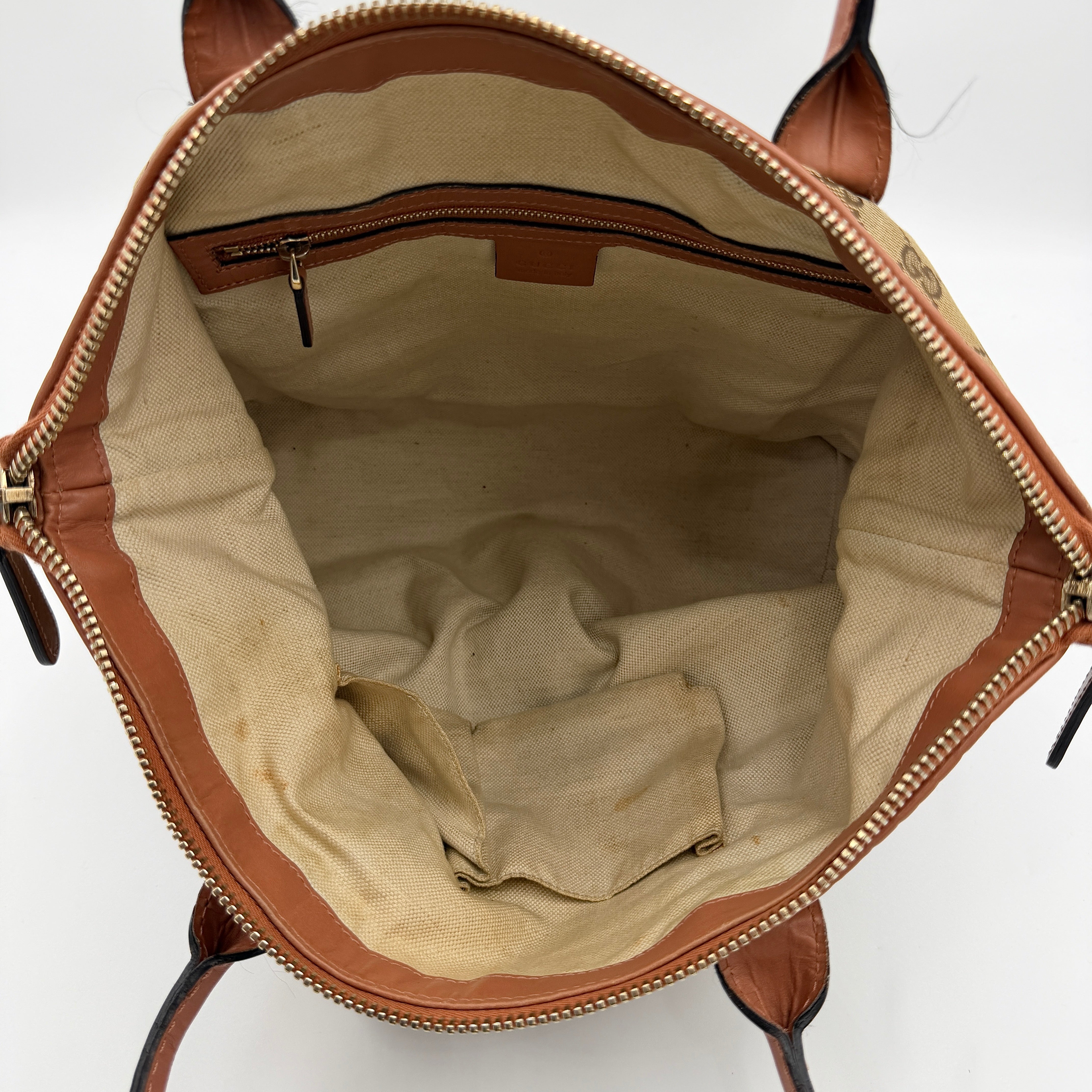 Gucci beige GG monogram shoulder bag with orange leather trim, heart bit charm, and detachable strap displayed on a white background.