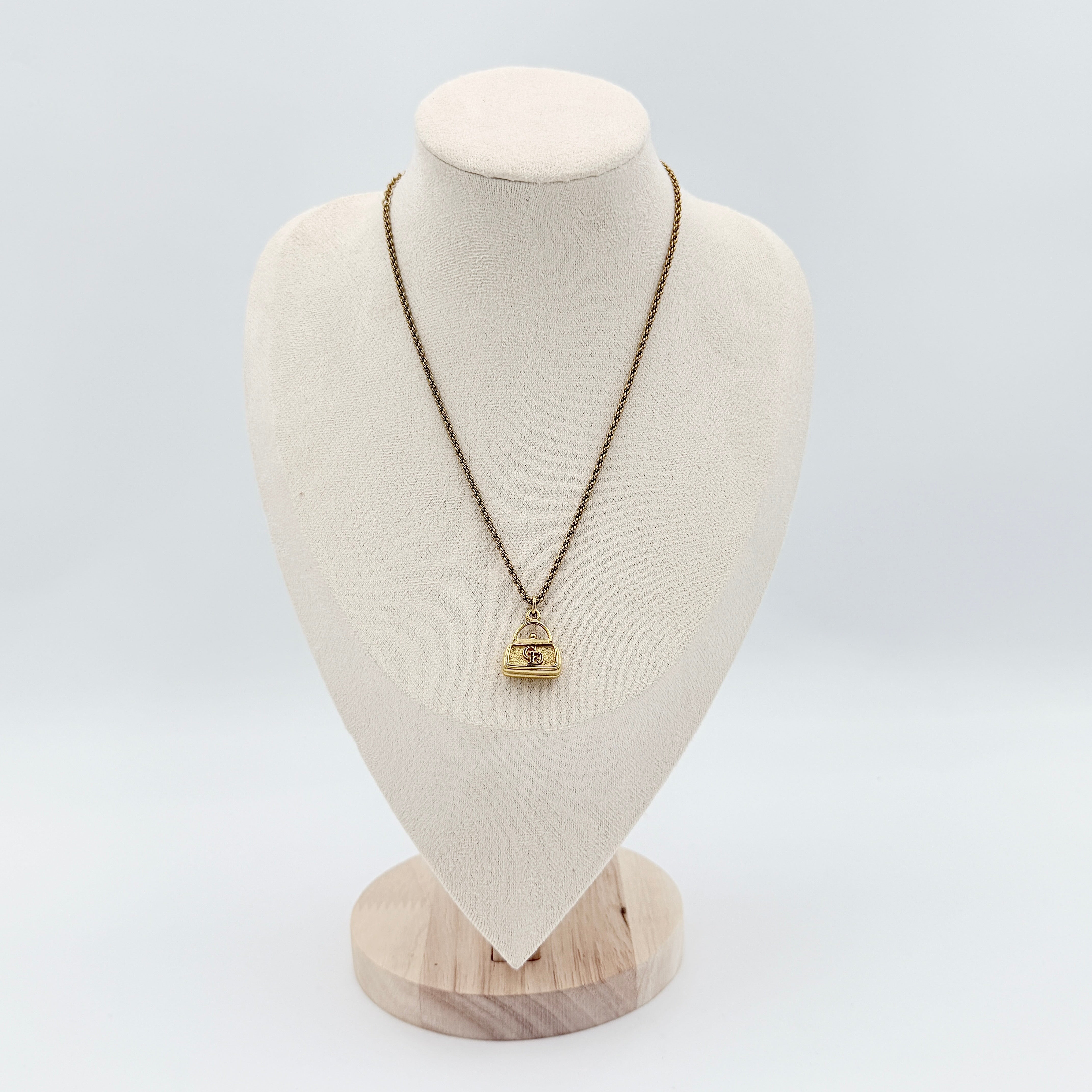 Dior gold necklace with a CD logo handbag pendant on a twisted chain, shown laid flat against a white background.