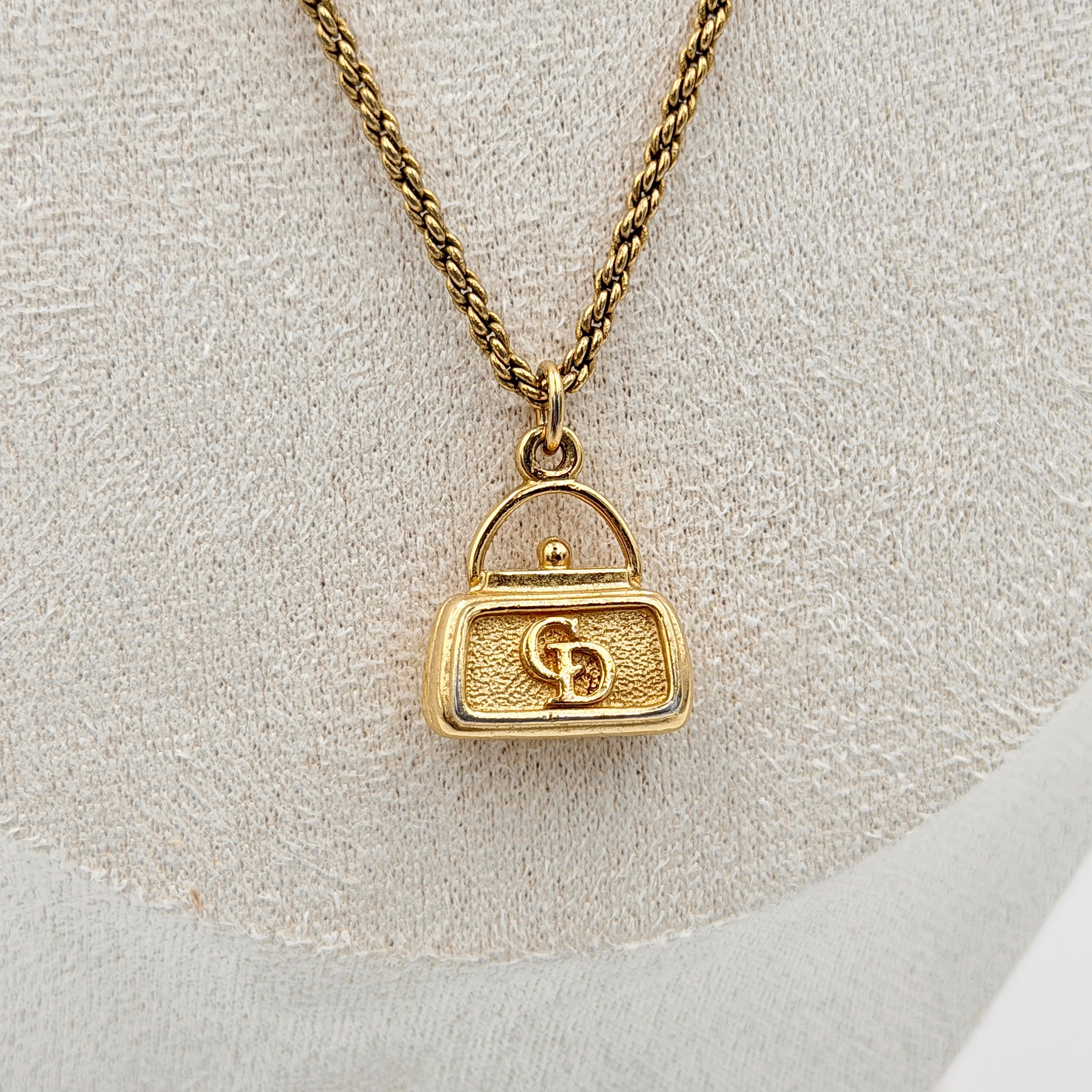 Dior gold necklace with a CD logo handbag pendant on a twisted chain, shown laid flat against a white background.