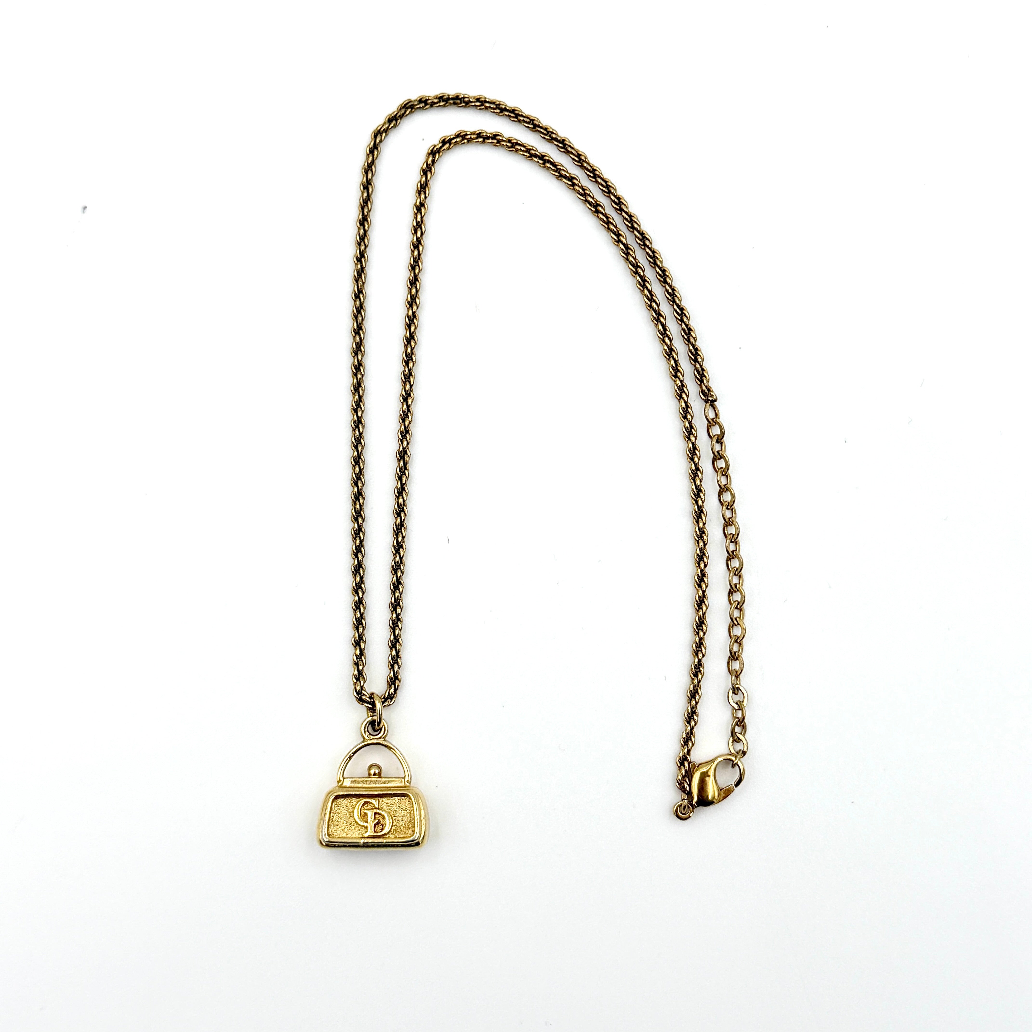 Dior gold necklace with a CD logo handbag pendant on a twisted chain, shown laid flat against a white background.