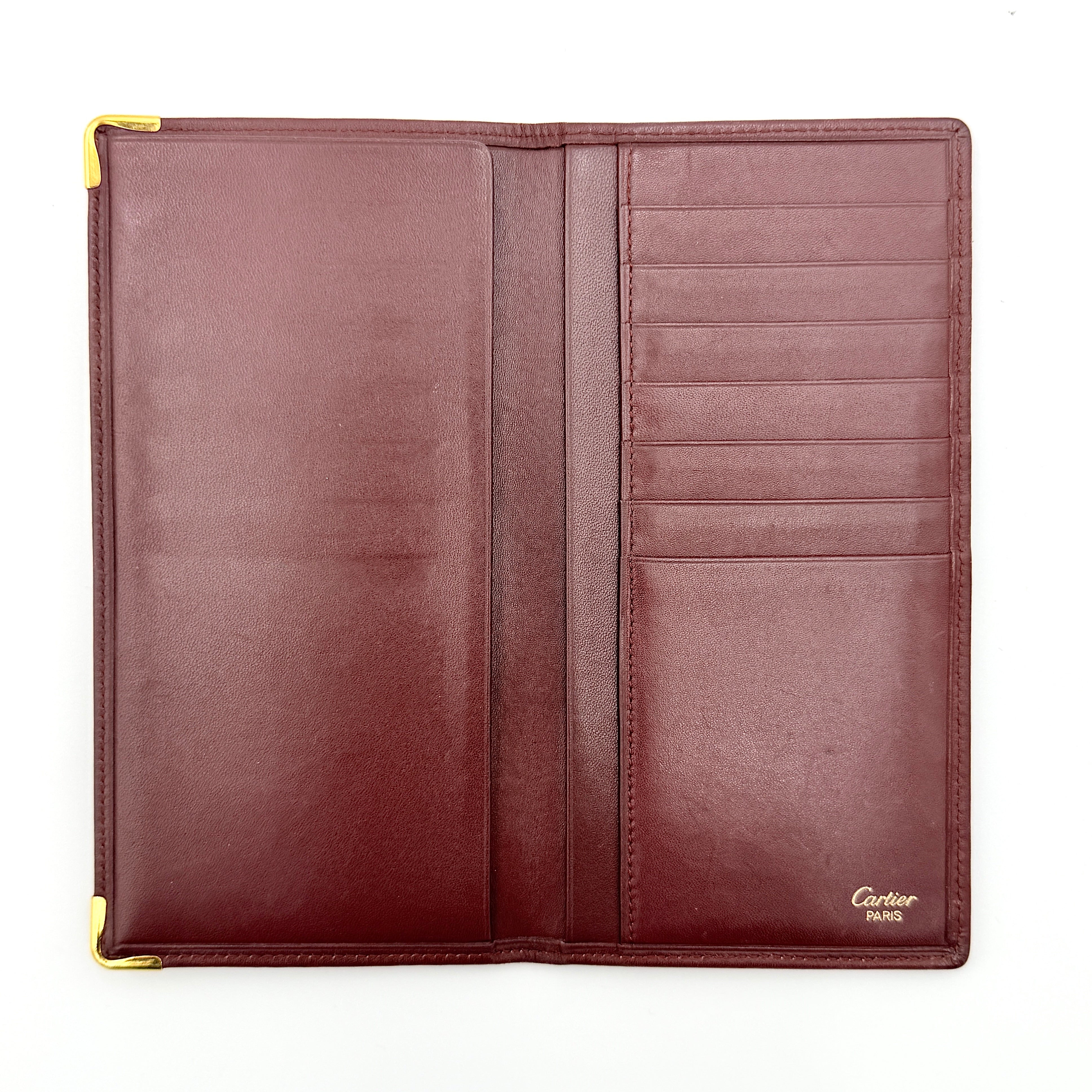 The Cartier Must de Cartier long bifold wallet in rich bordeaux calfskin with gold-tone corner accents and an embossed logo.