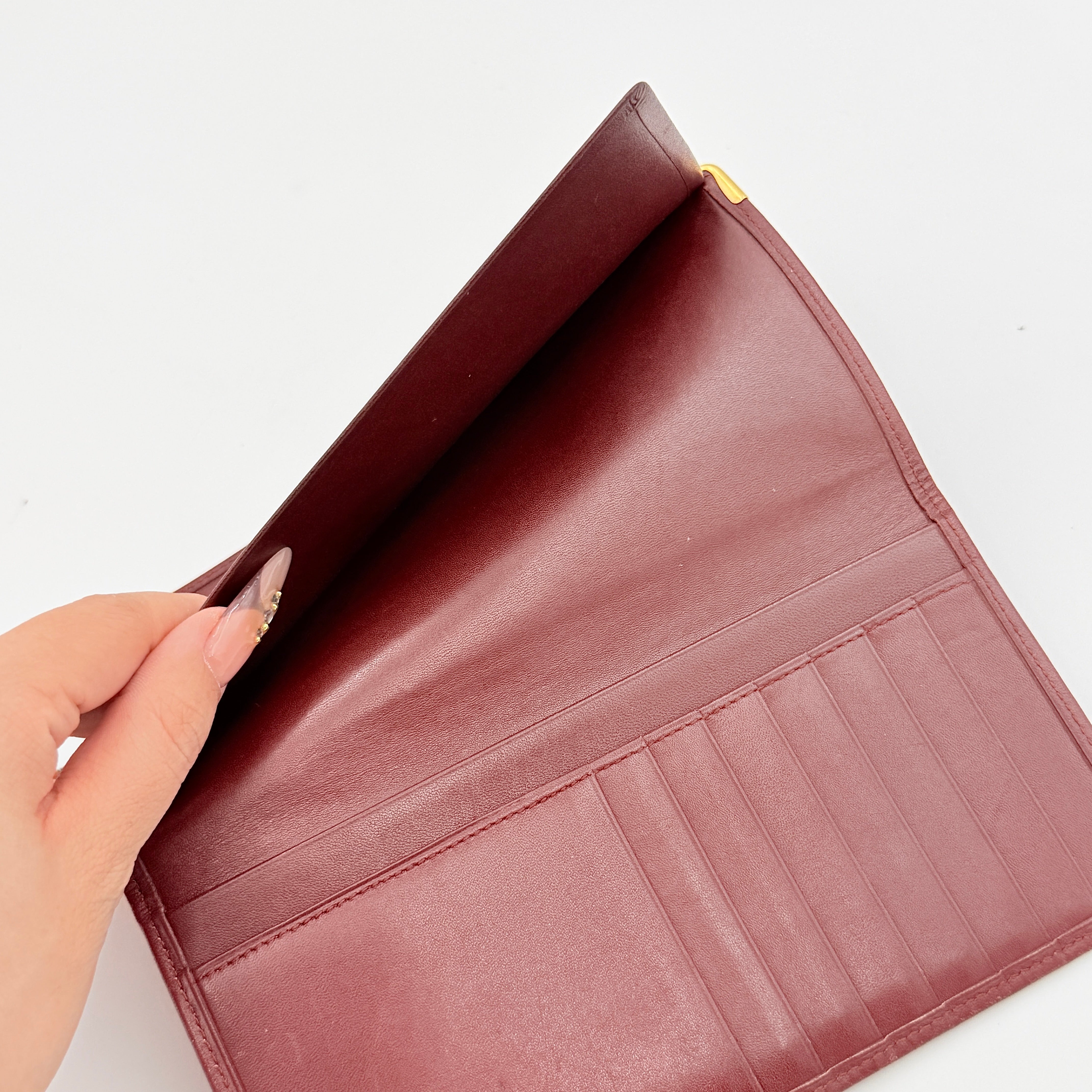 The Cartier Must de Cartier long bifold wallet in rich bordeaux calfskin with gold-tone corner accents and an embossed logo.