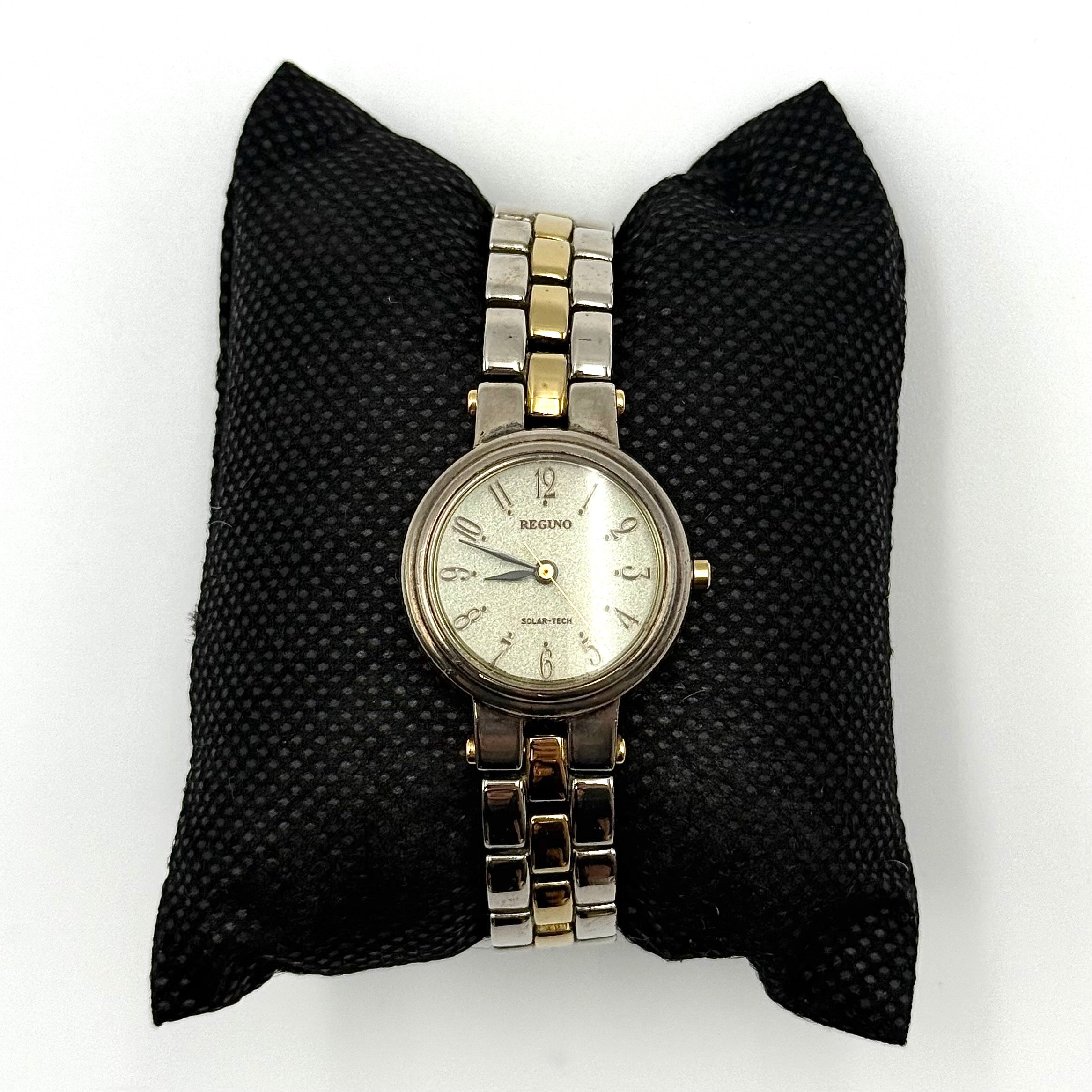 Citizen Reguno two-tone stainless steel watch in gold and silver with a round dial and linked bracelet, displayed on a black pillow.