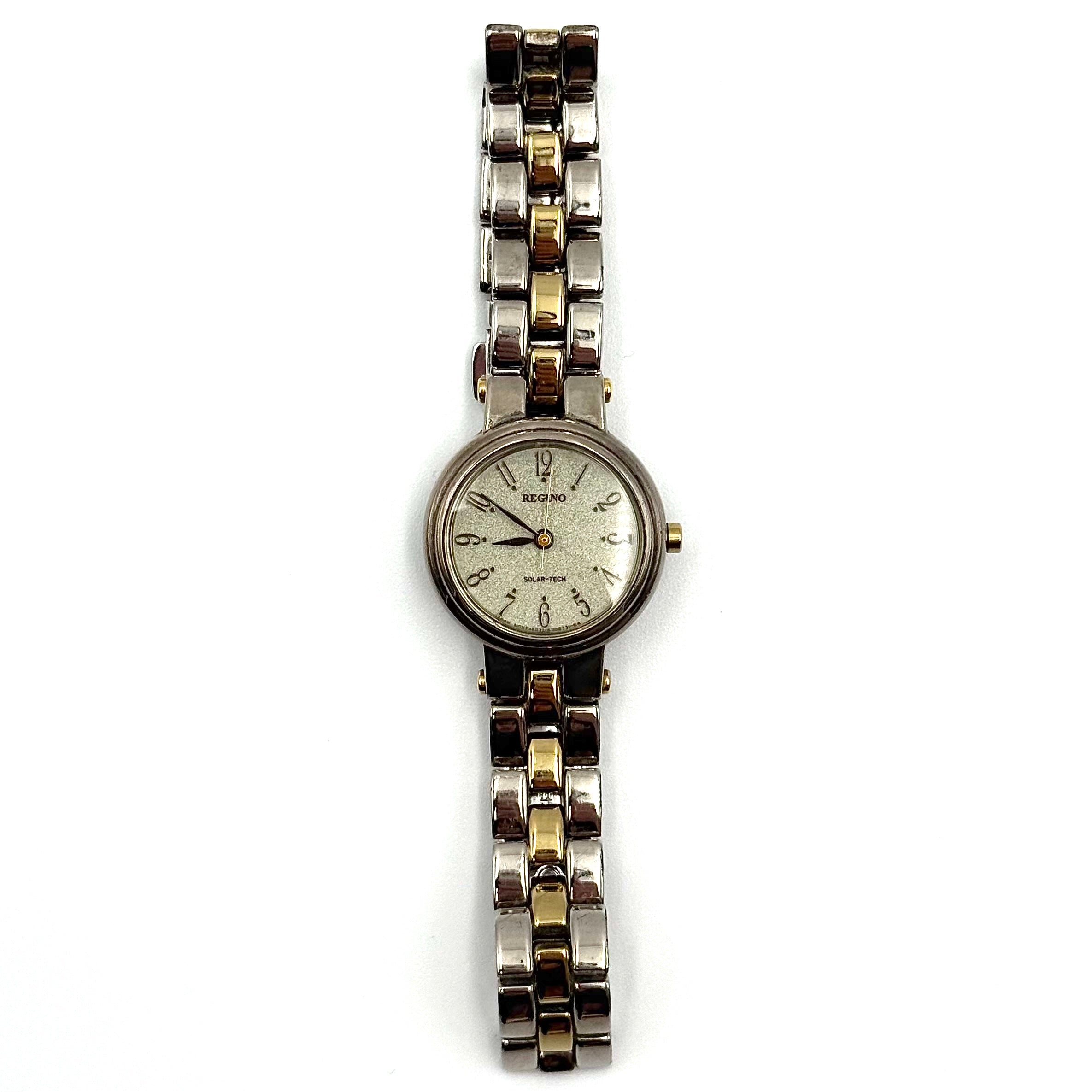 Citizen Reguno two-tone stainless steel watch in gold and silver with a round dial and linked bracelet, displayed on a black pillow.