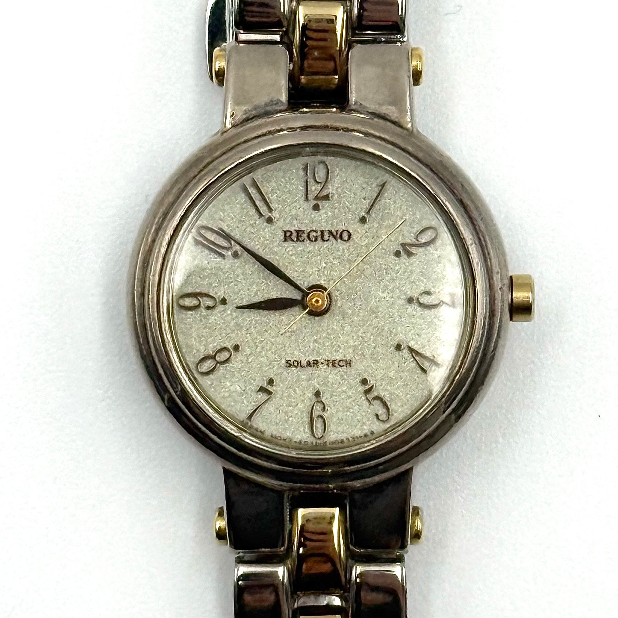 Citizen Reguno two-tone stainless steel watch in gold and silver with a round dial and linked bracelet, displayed on a black pillow.