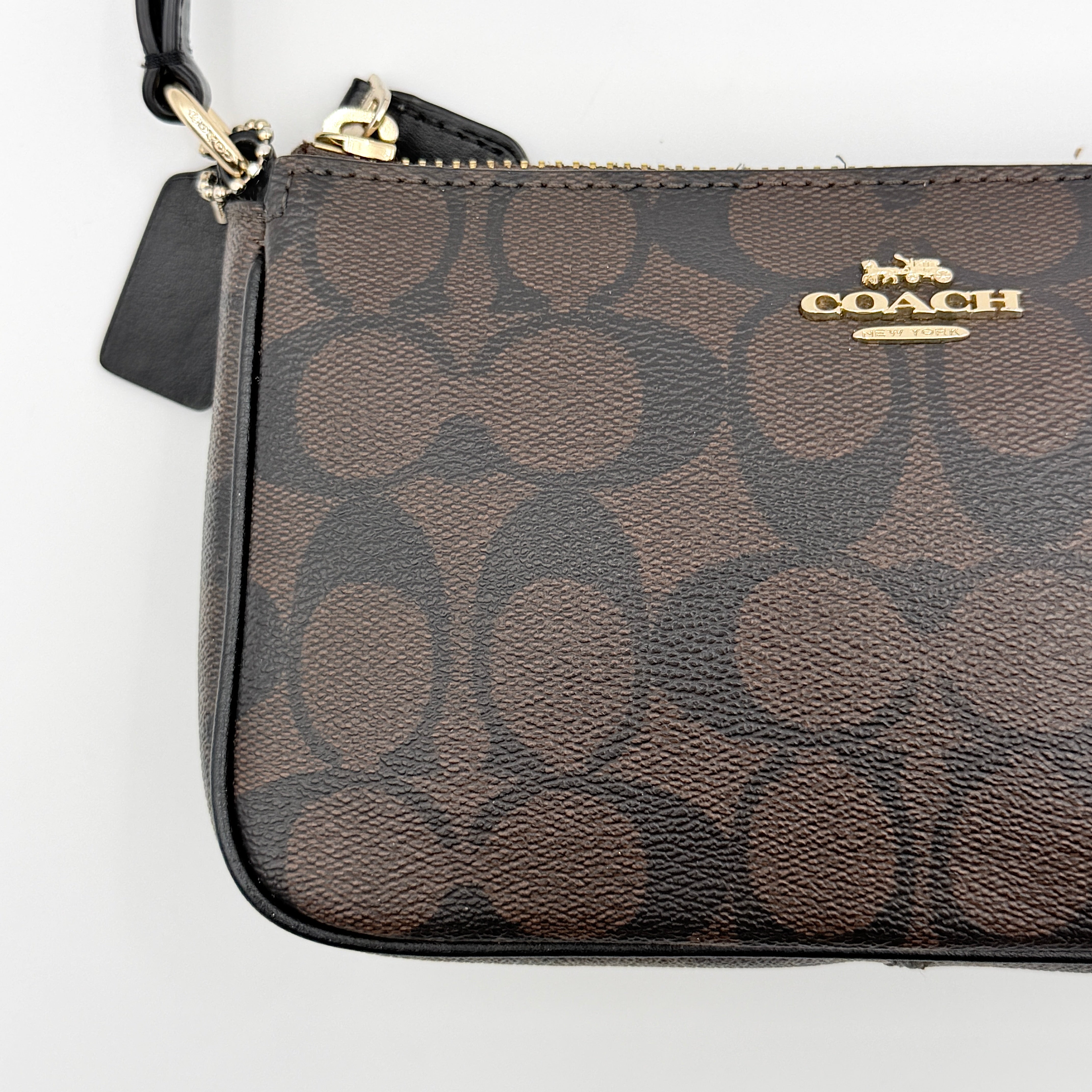 Coach Signature Nolita 19 shoulder bag in brown monogram canvas with black leather strap and gold-tone hardware, shown against a white background.