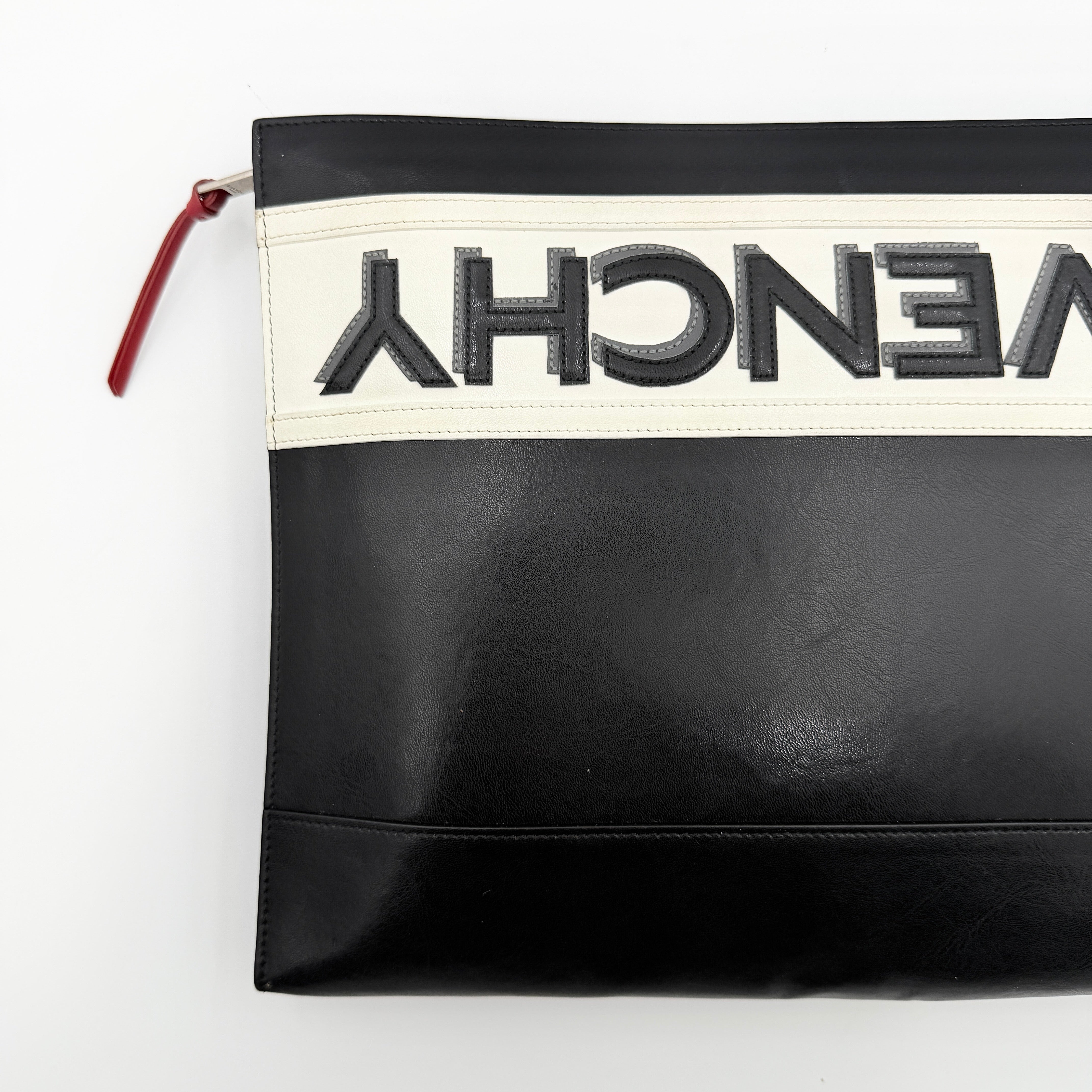 Front view of a Givenchy black leather clutch with bold white logo panel and red zip pull.