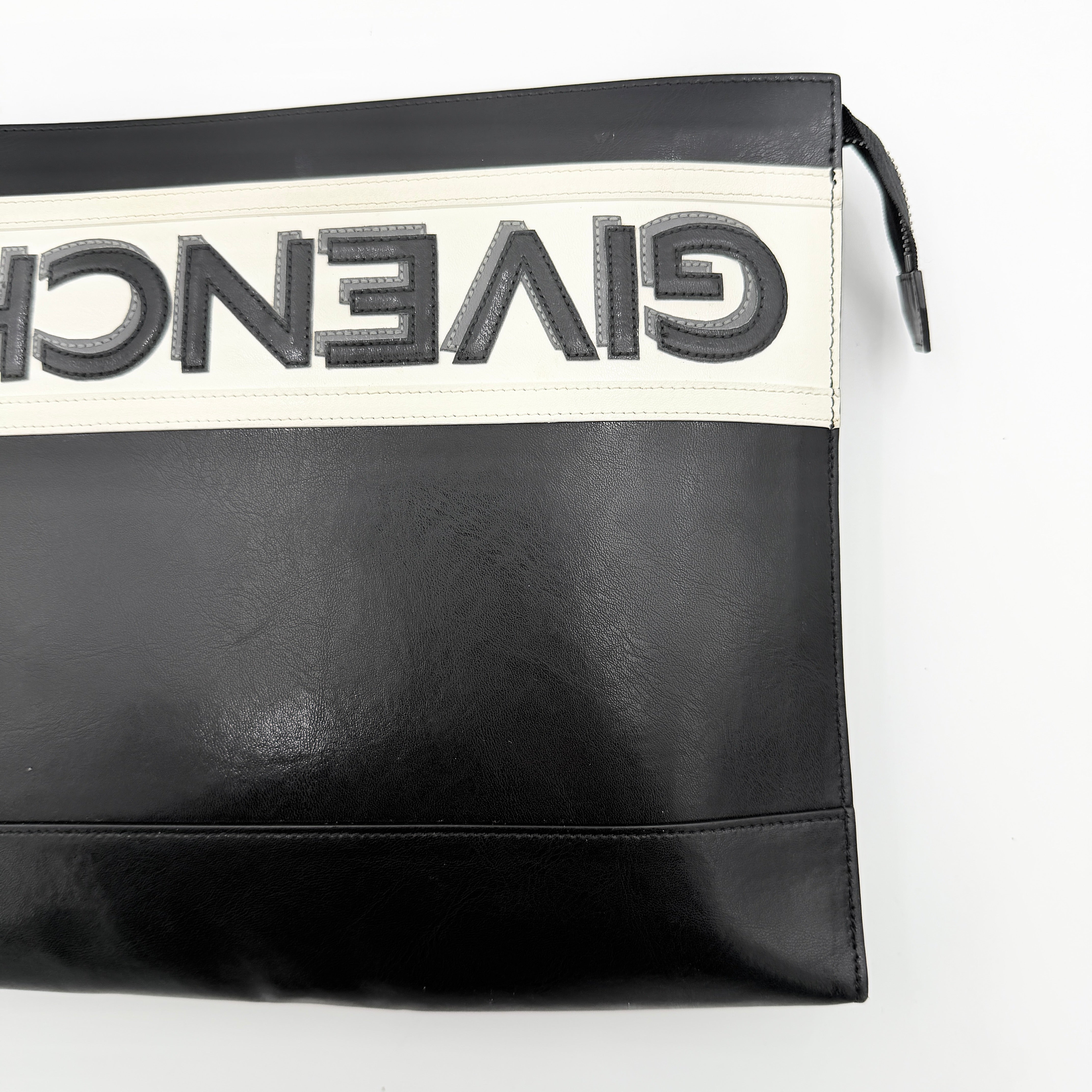 Front view of a Givenchy black leather clutch with bold white logo panel and red zip pull.