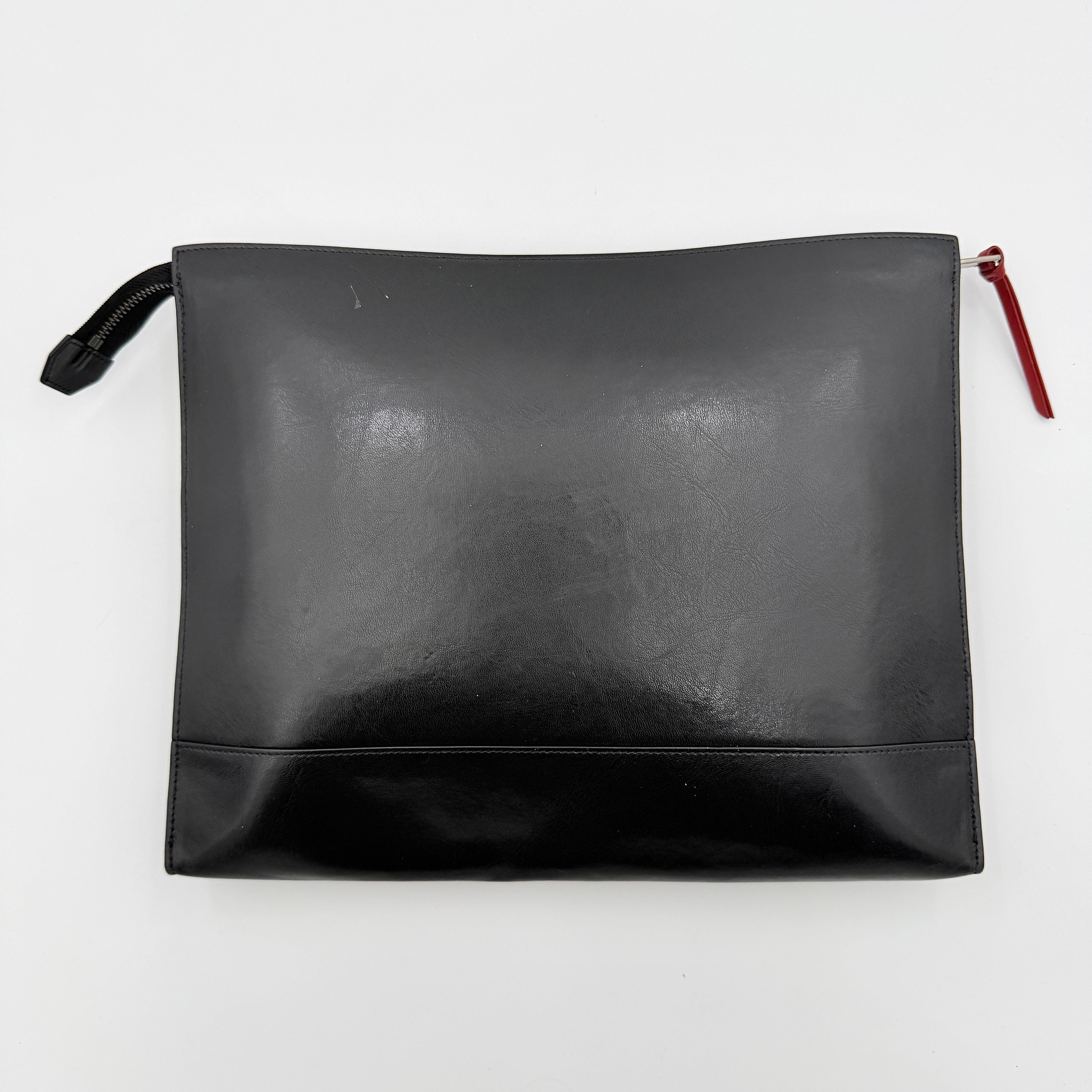 Front view of a Givenchy black leather clutch with bold white logo panel and red zip pull.