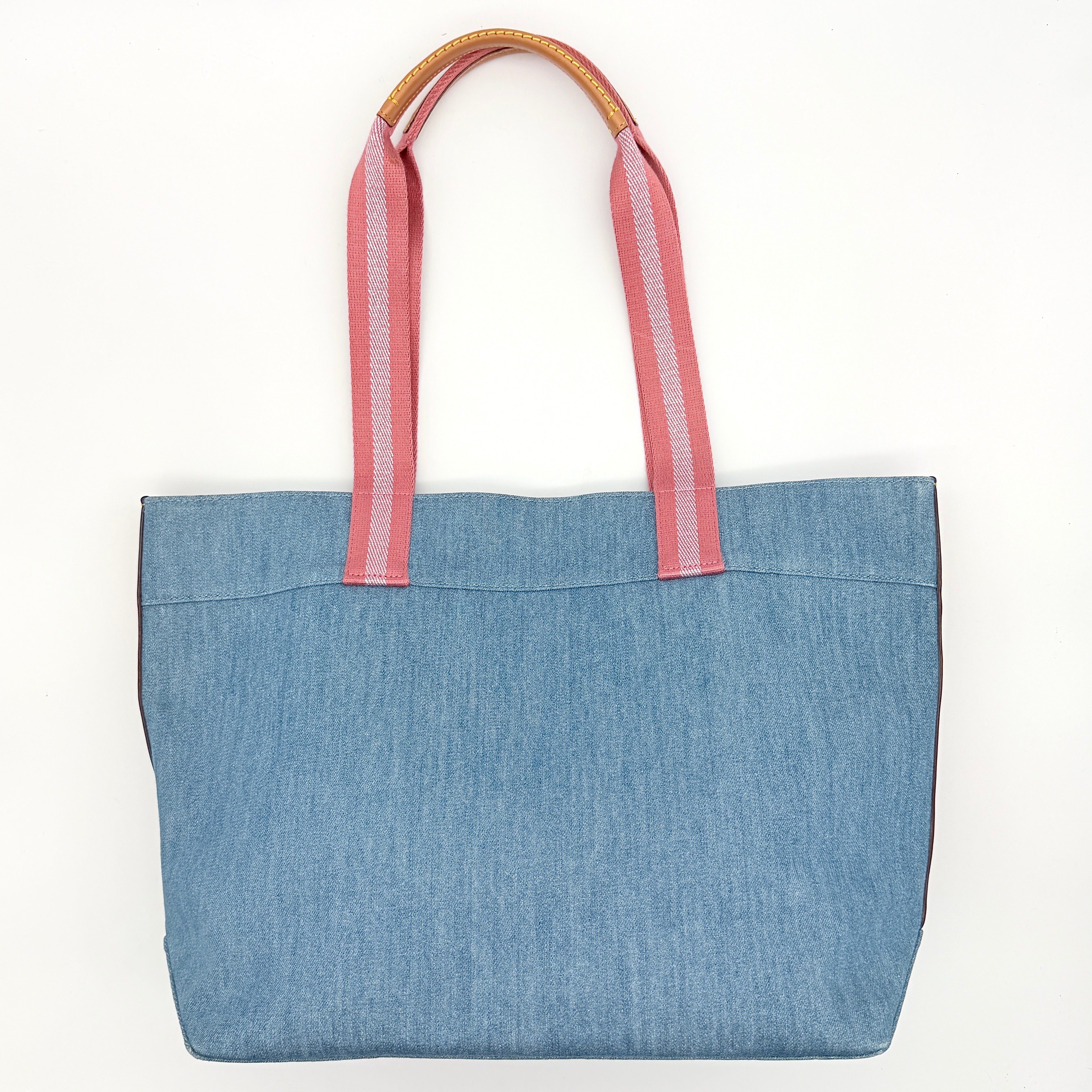 Coach denim tote bag with pink handles and a white flower and hang tag graphic at the corner