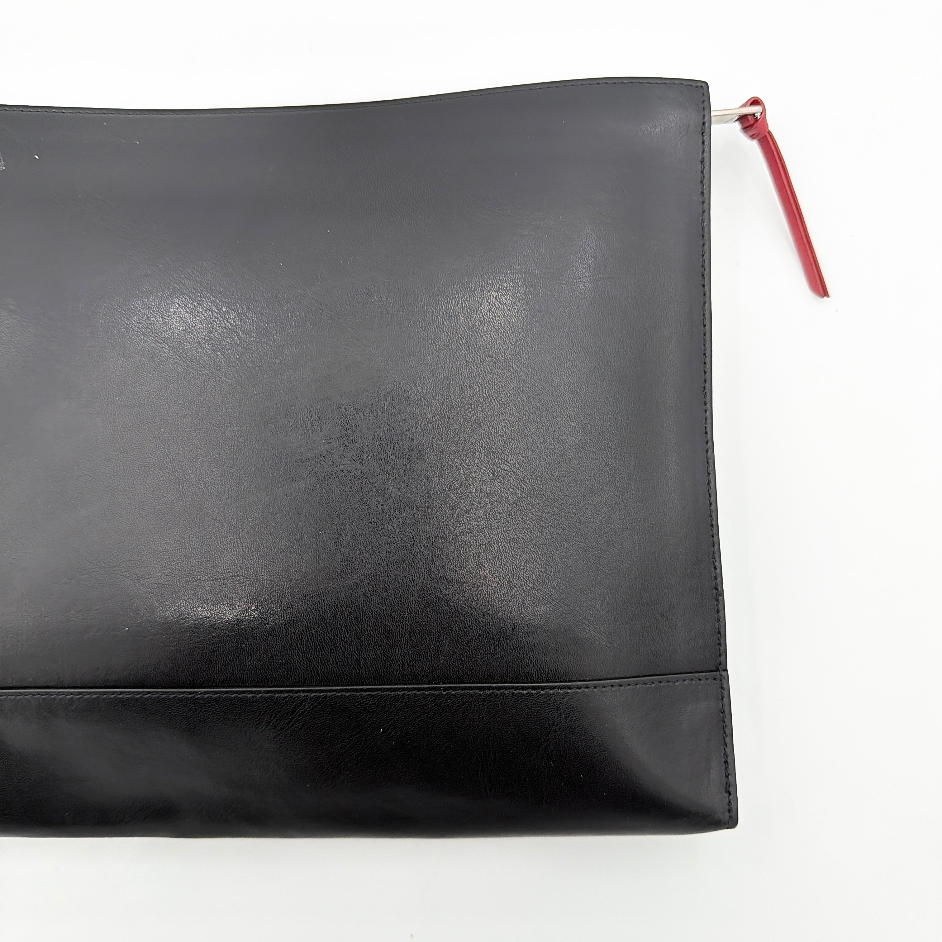 Front view of a Givenchy black leather clutch with bold white logo panel and red zip pull.