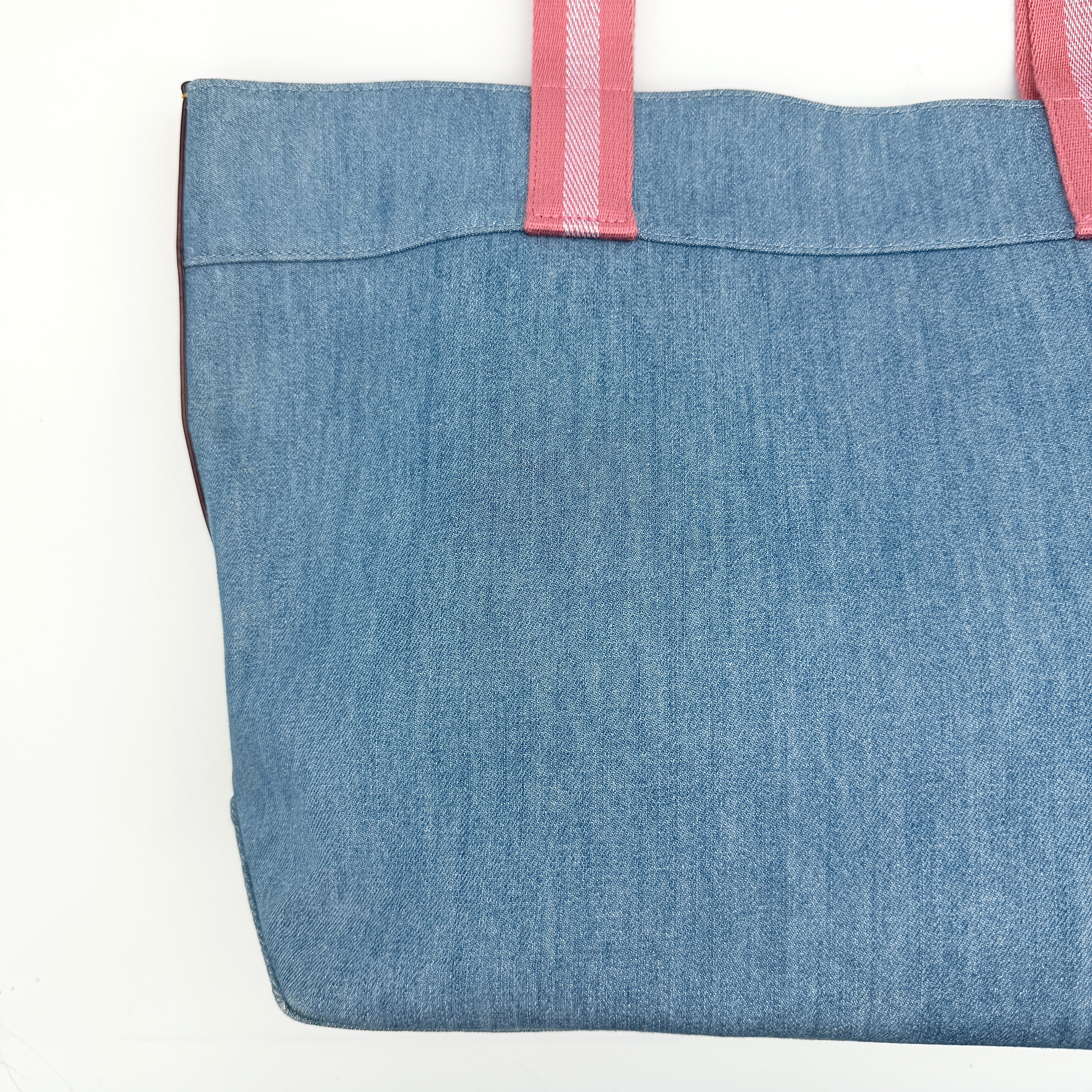 Coach denim tote bag with pink handles and a white flower and hang tag graphic at the corner