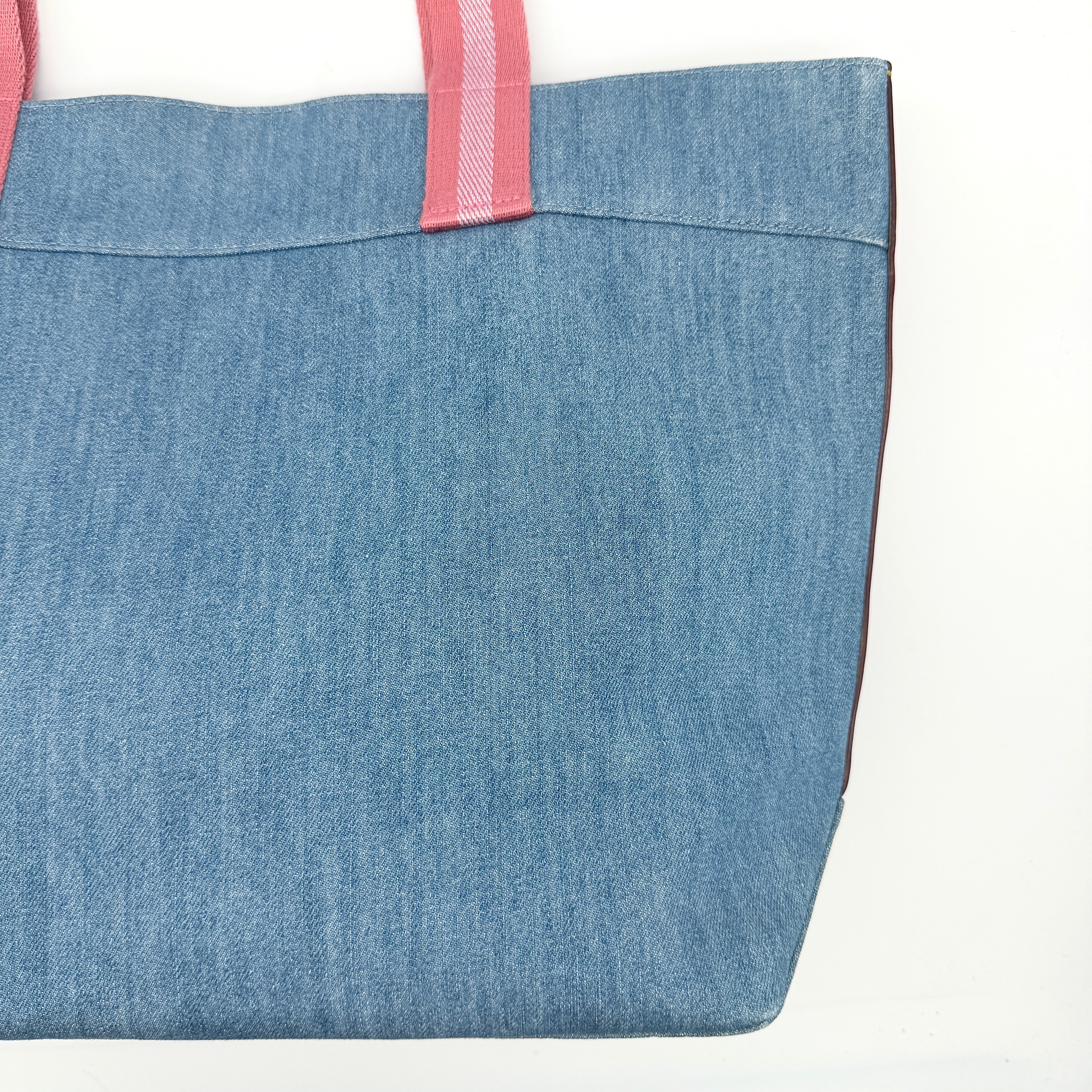 Coach denim tote bag with pink handles and a white flower and hang tag graphic at the corner