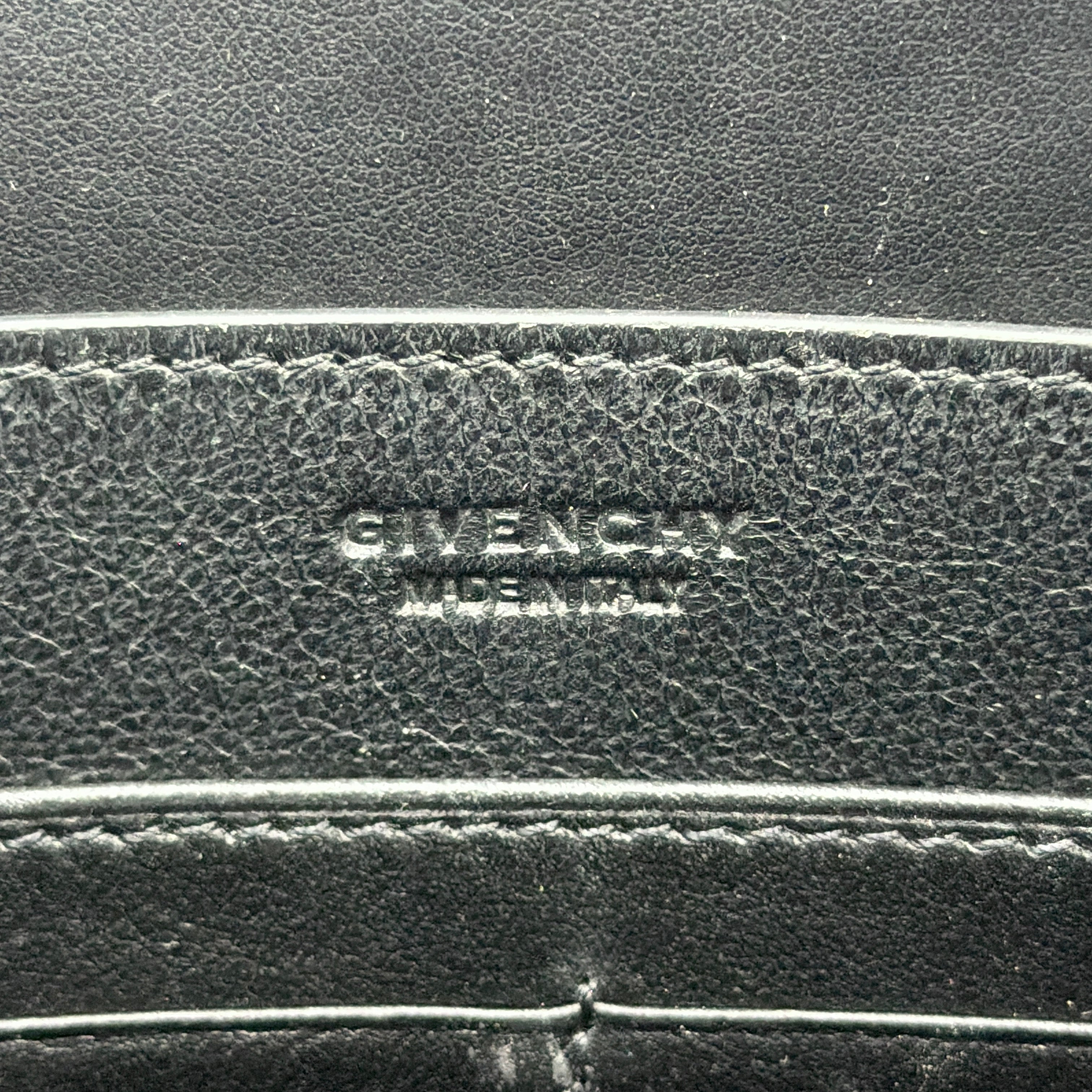 Front view of a Givenchy black leather clutch with bold white logo panel and red zip pull.