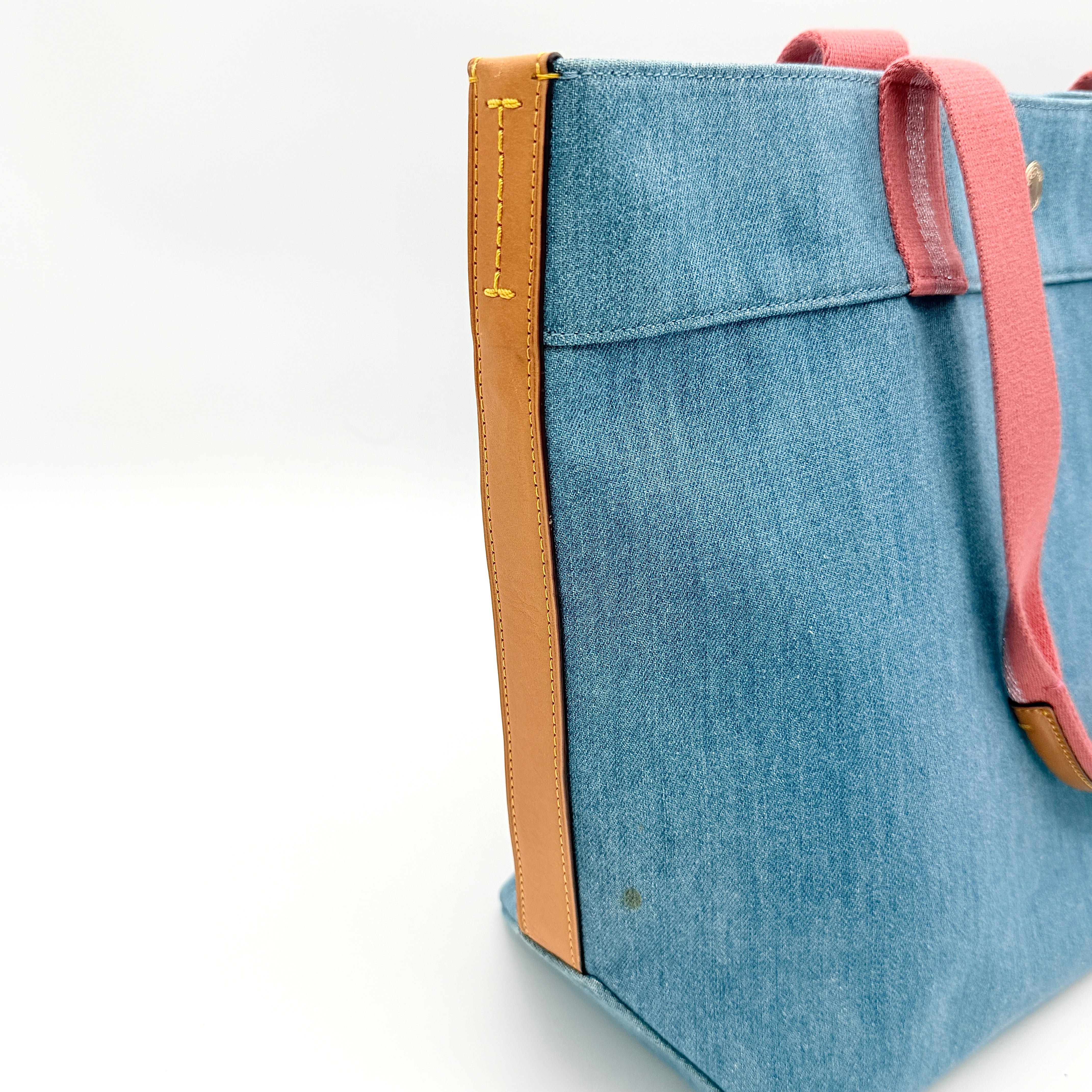 Coach denim tote bag with pink handles and a white flower and hang tag graphic at the corner