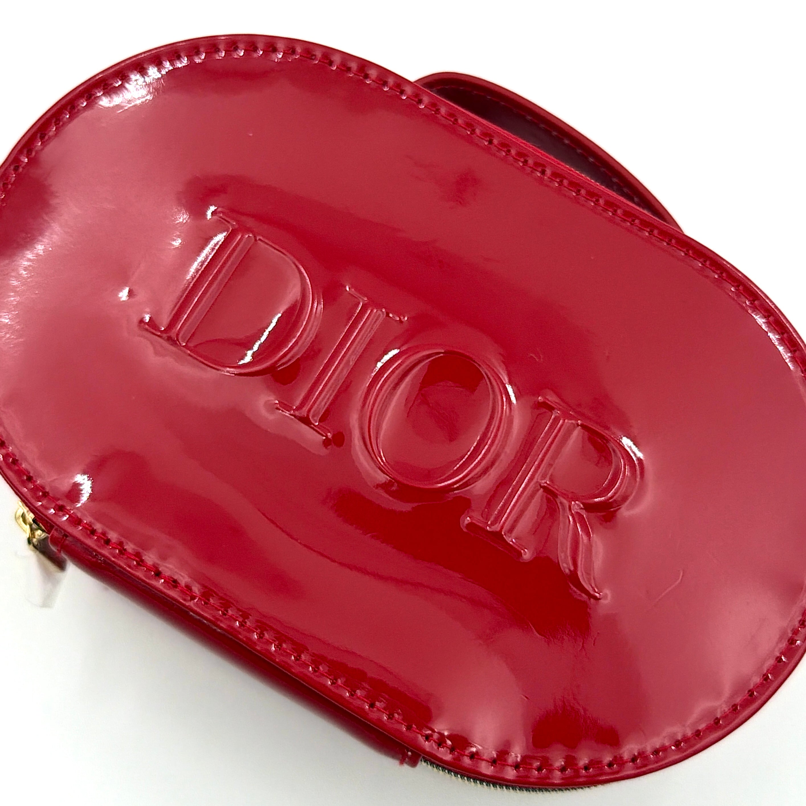 Christian Dior patent leather cosmetic pouch in glossy red with embossed DIOR logo and gold zip hardware.