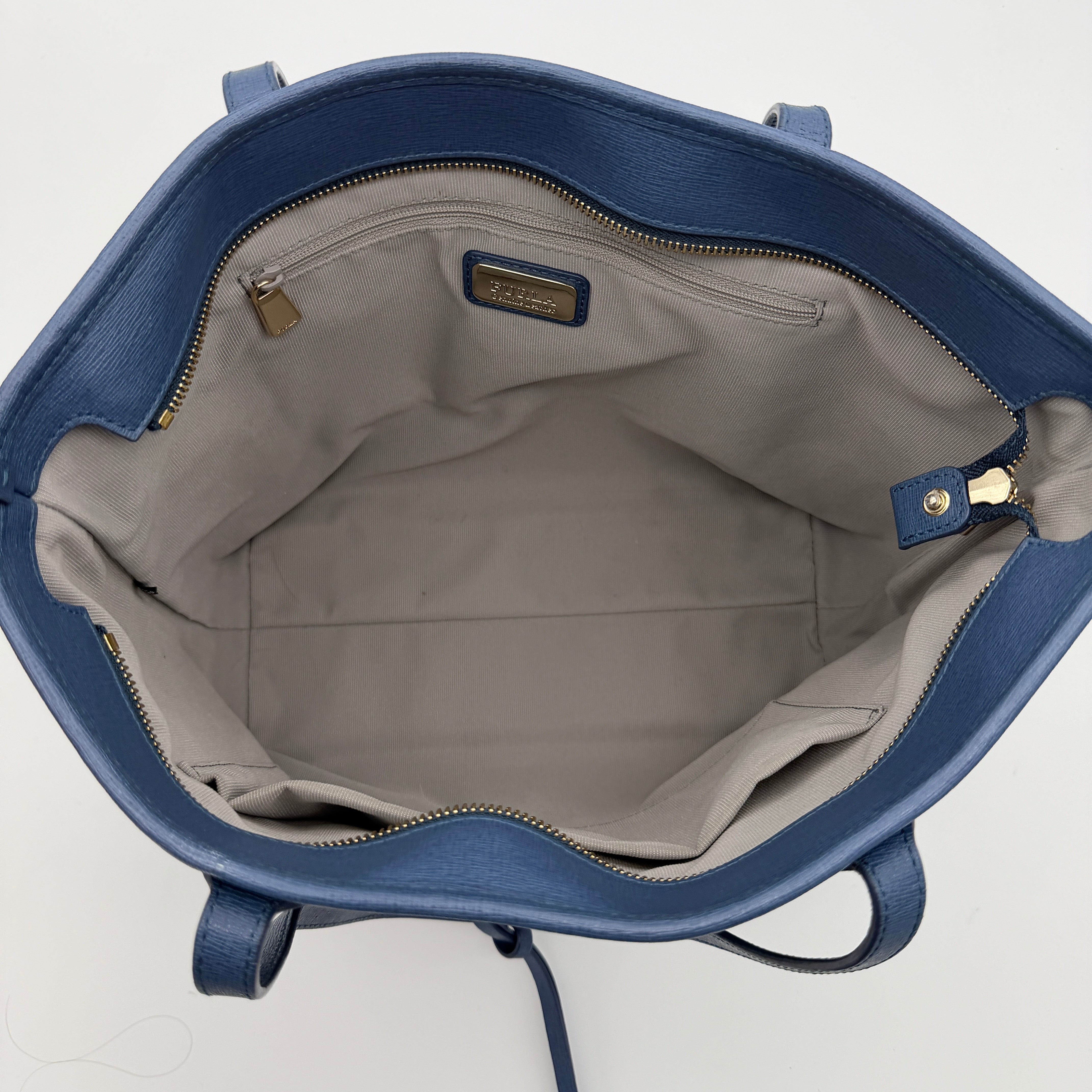 Furla New Daisy Tote Bag in blue leather with gold-tone logo charm and double handles, displayed against a white background
