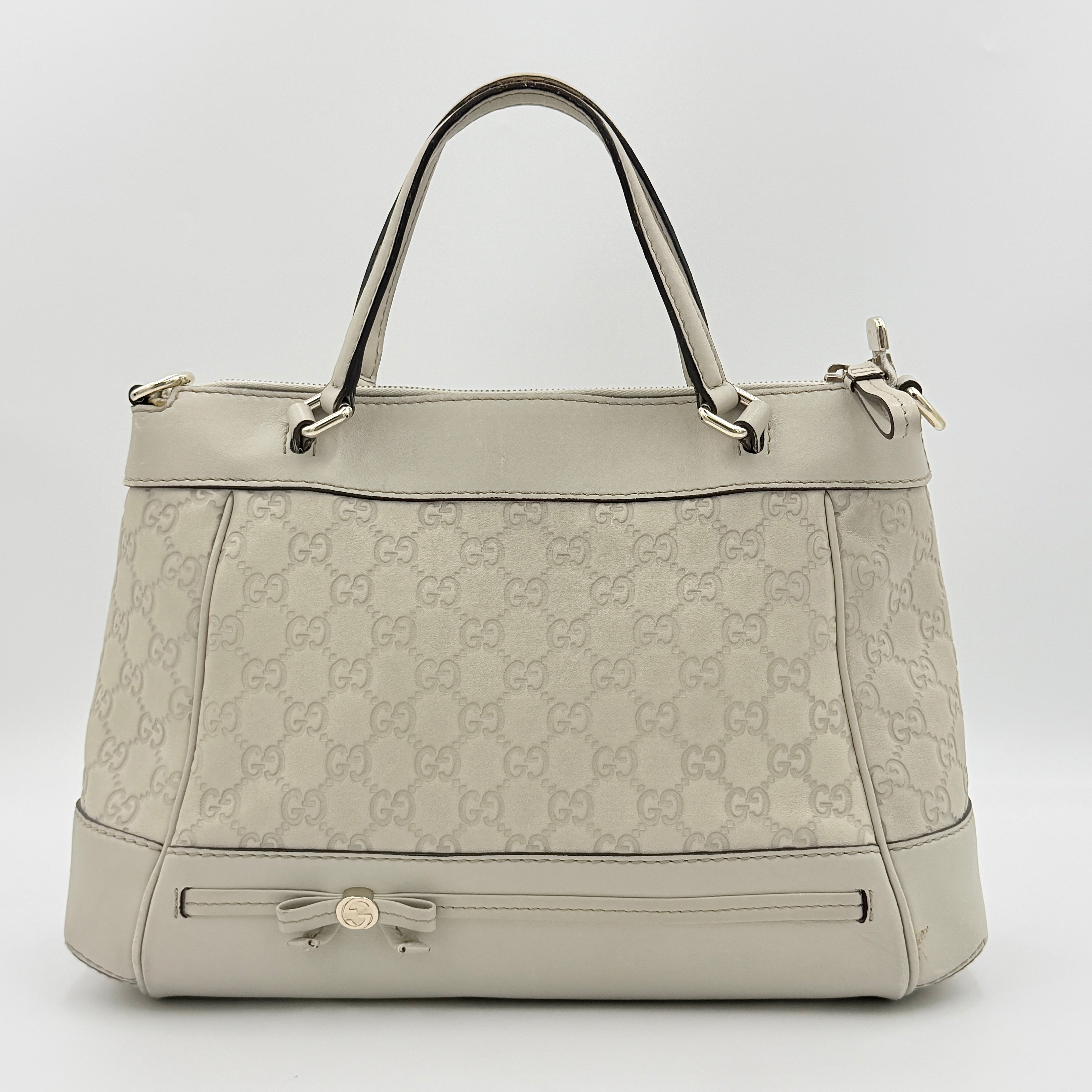 Gucci Mayfair Bow 2Way shoulder bag in cream GG monogram leather with dual handles and detachable strap, styled against a neutral backdrop.