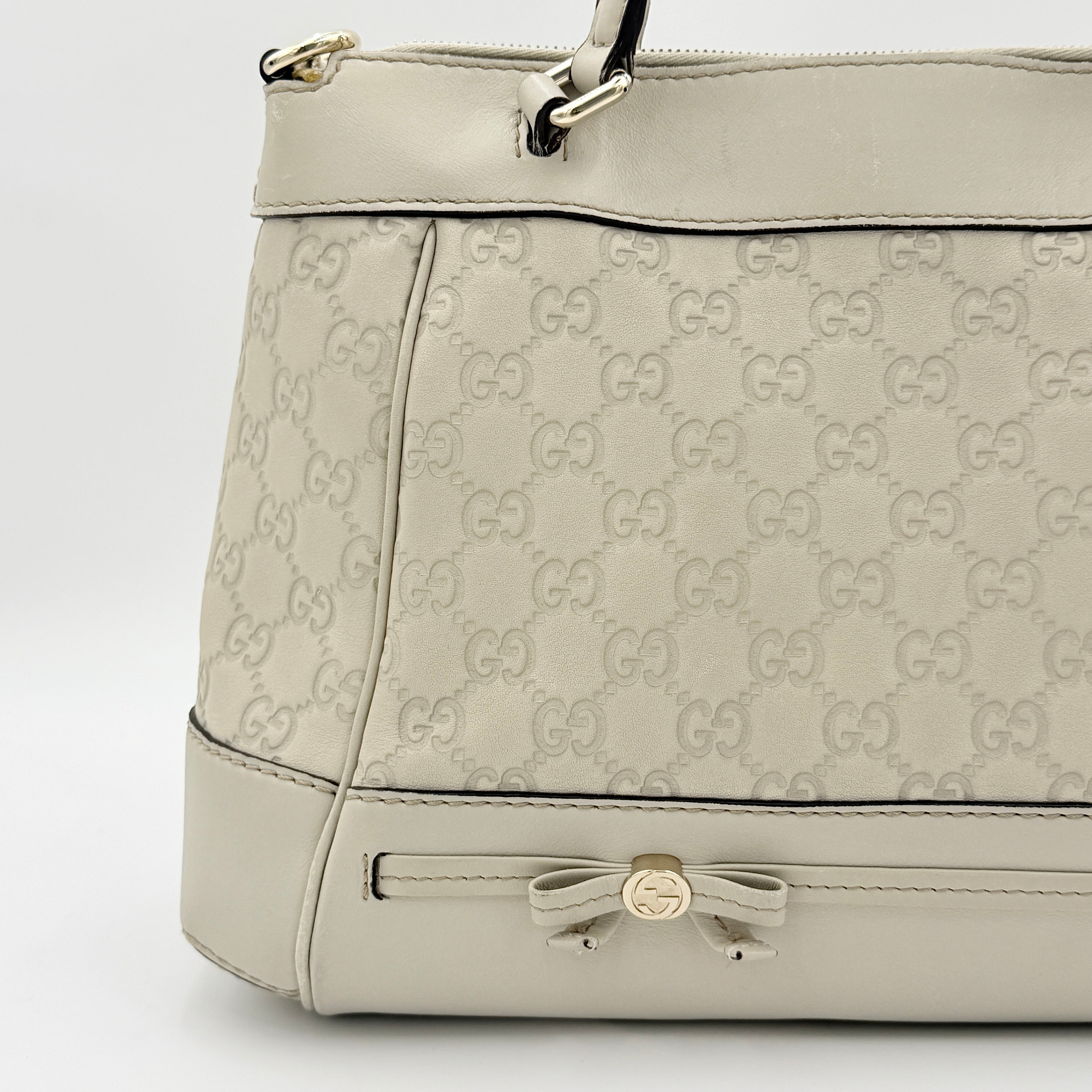 Gucci Mayfair Bow 2Way shoulder bag in cream GG monogram leather with dual handles and detachable strap, styled against a neutral backdrop.