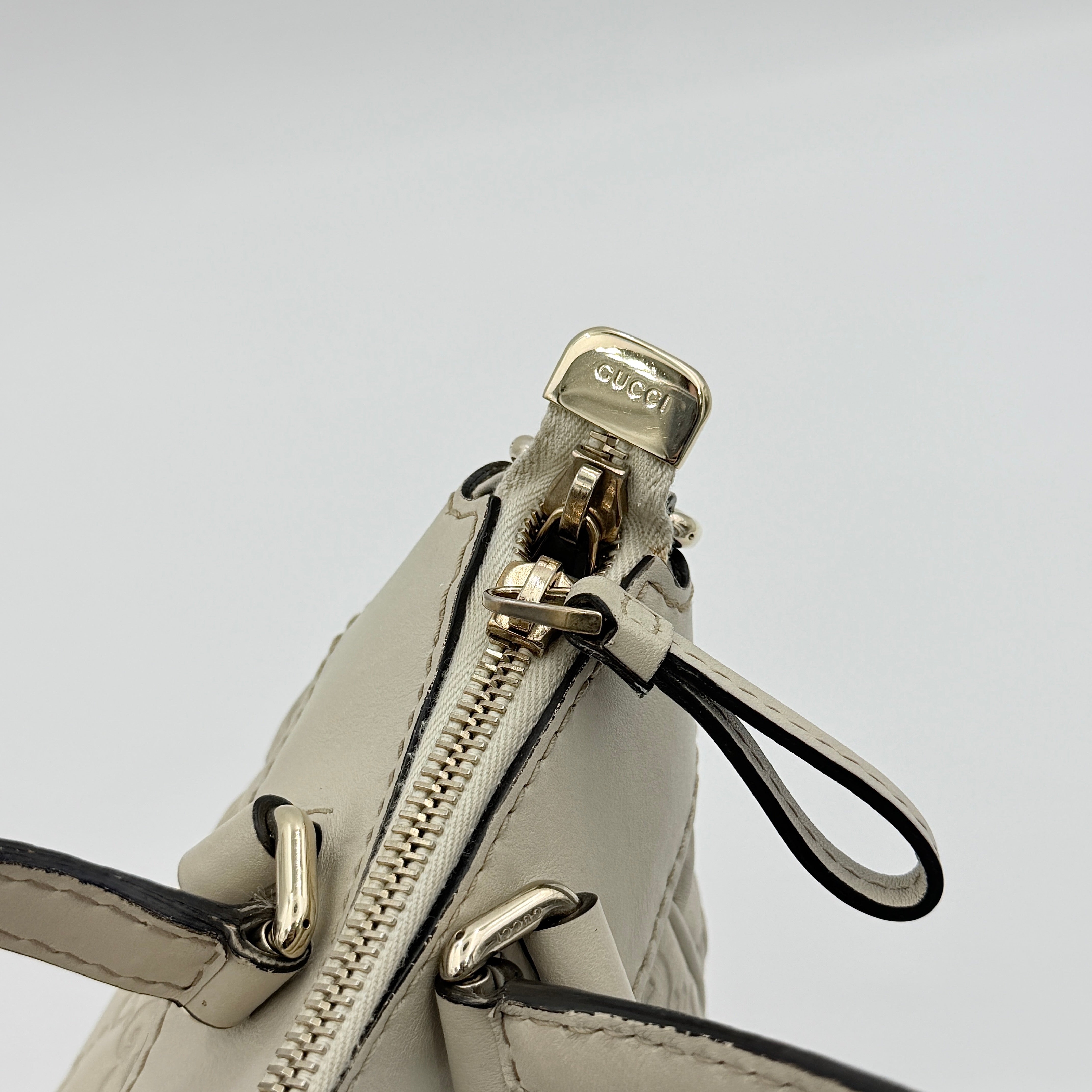 Gucci Mayfair Bow 2Way shoulder bag in cream GG monogram leather with dual handles and detachable strap, styled against a neutral backdrop.