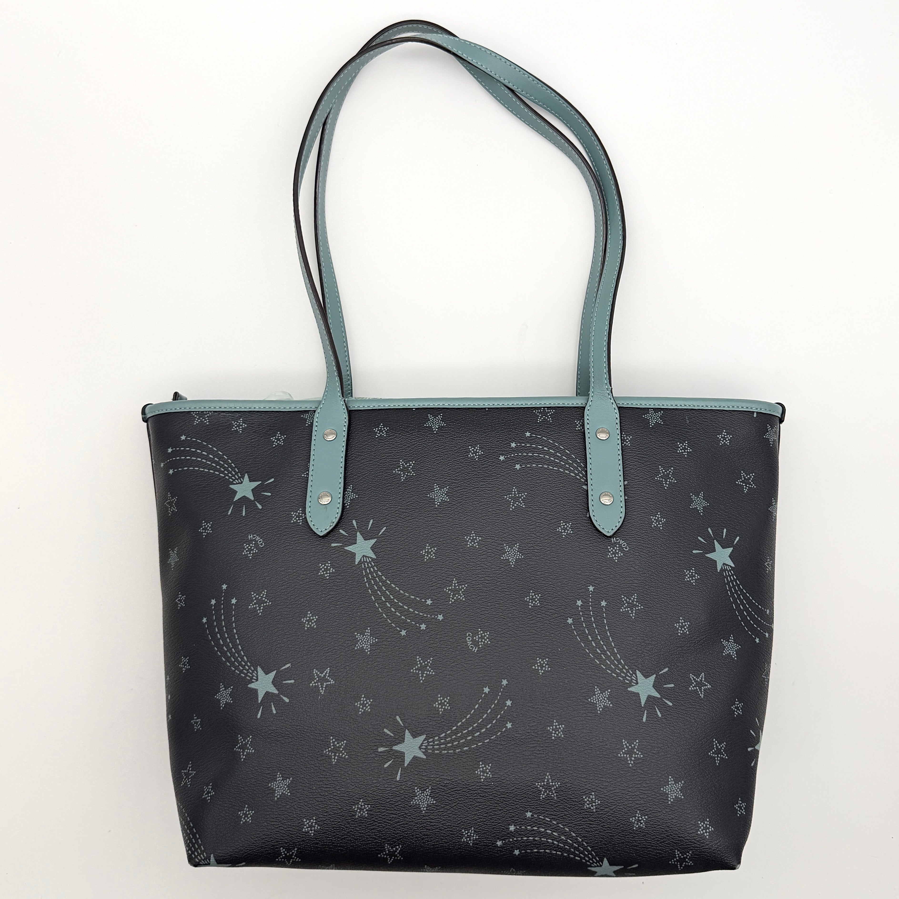 Coach Fiona Zip Tote in navy blue with star print and blue leather handles against a white background.