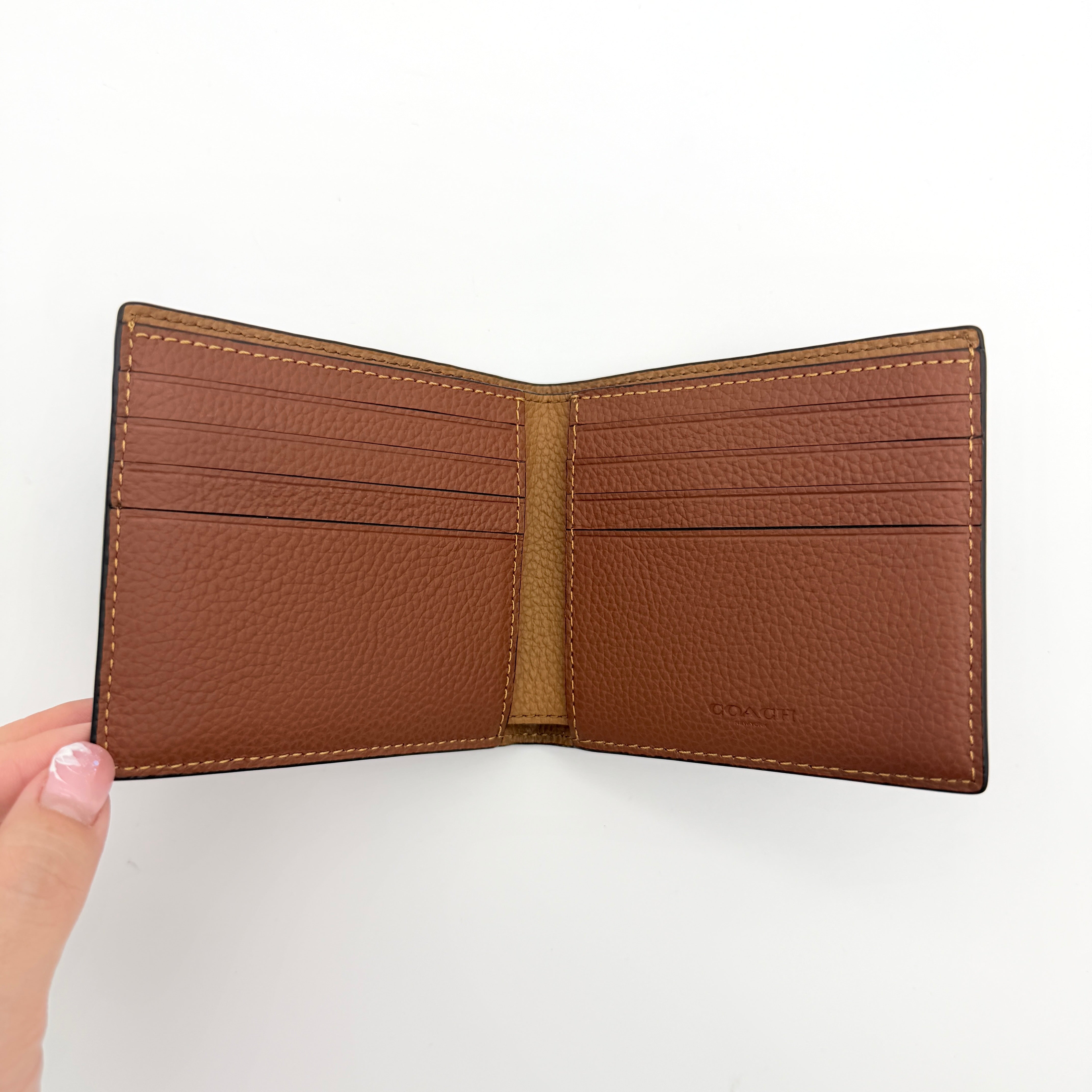 Coach slim billfold wallet in saddle brown pebbled leather with embossed logo and refined topstitch detailing.