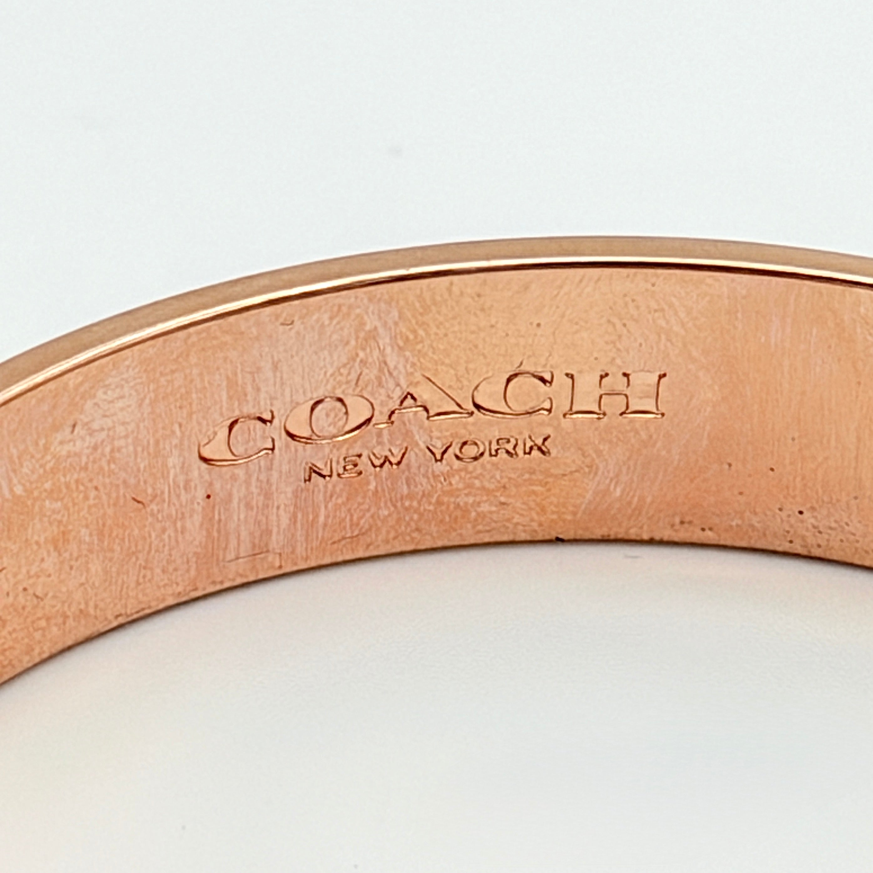 Coach rose gold bangle bracelet with signature enamel design, photographed with original box.