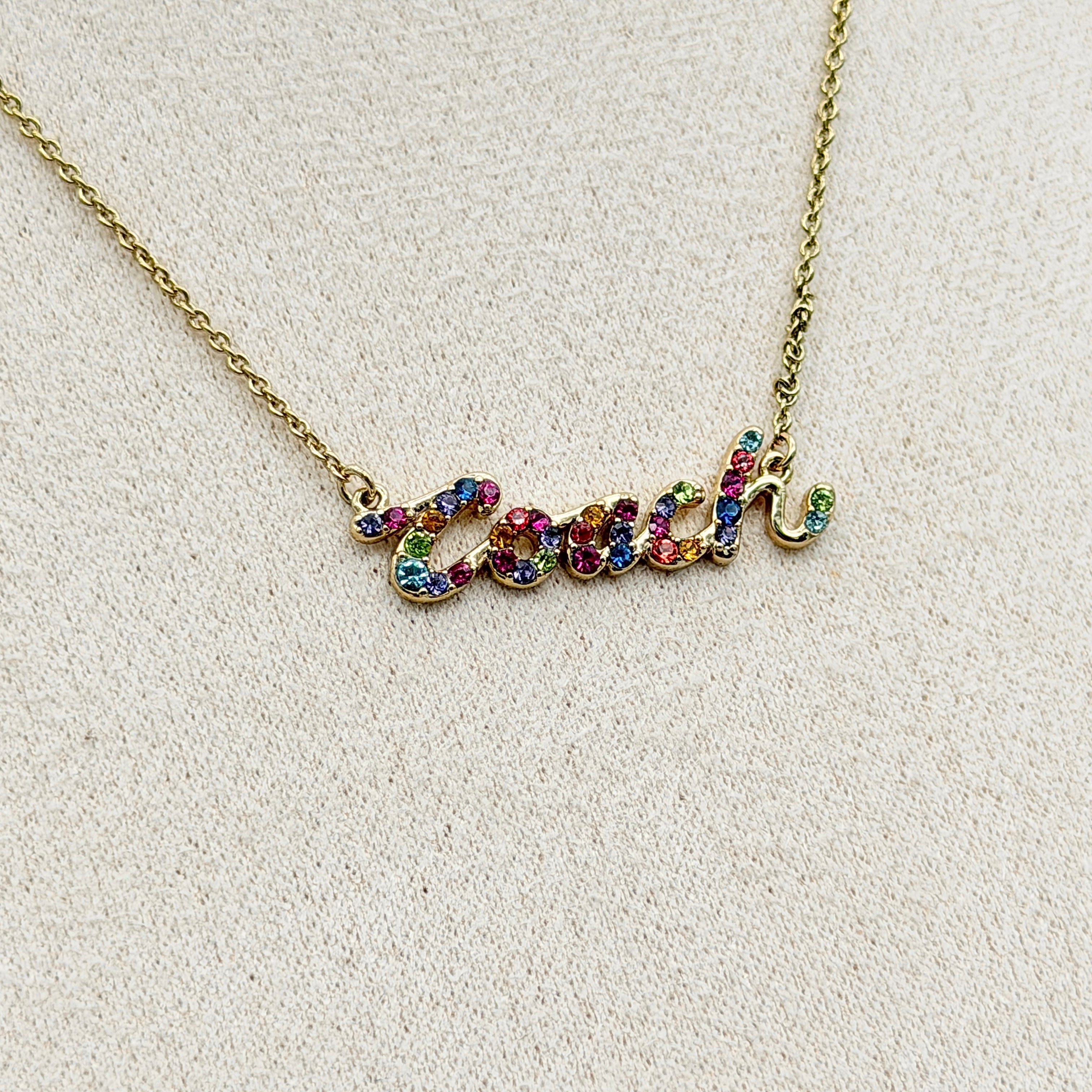 Coach Signature Script Rainbow Necklace with multicolour crystals set on a gold-tone chain, displayed in its original Coach box.
