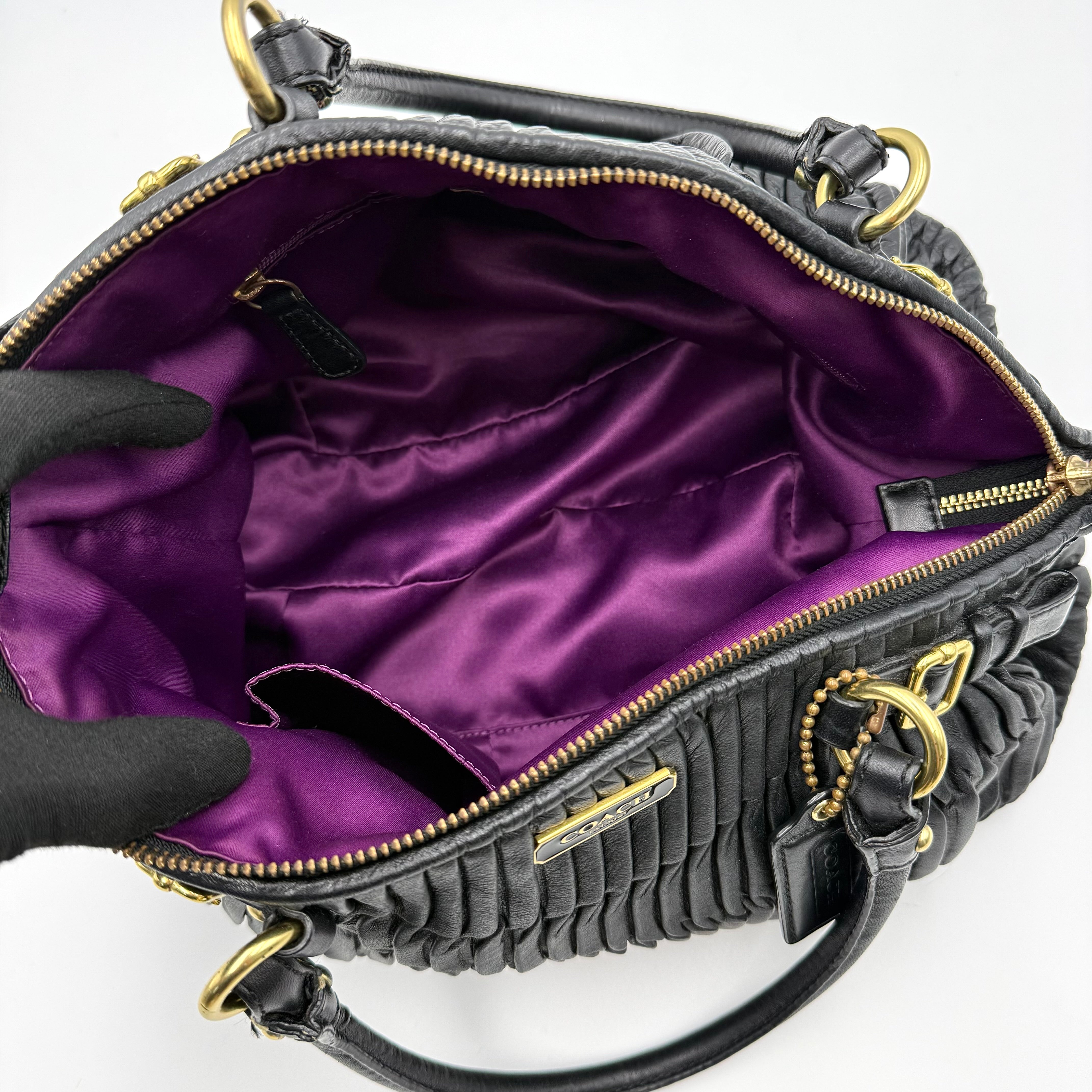 Coach Signature Madison shoulder bag in pleated black leather with gold hardware and dual handles.