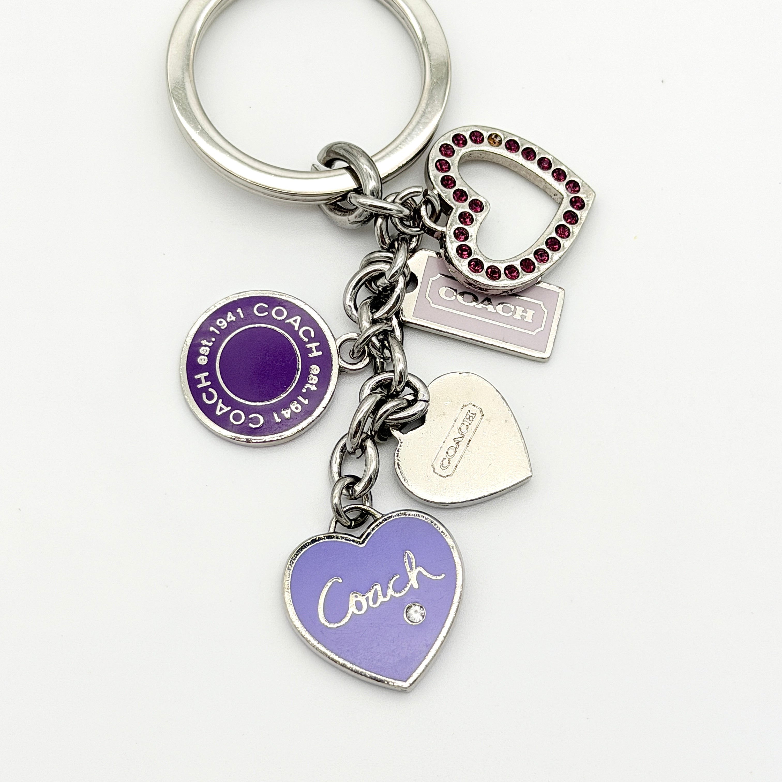 Coach Triple Heart Crystal Charms Keychain in purple and silver-tone, displayed on a Coach-branded drawstring pouch.