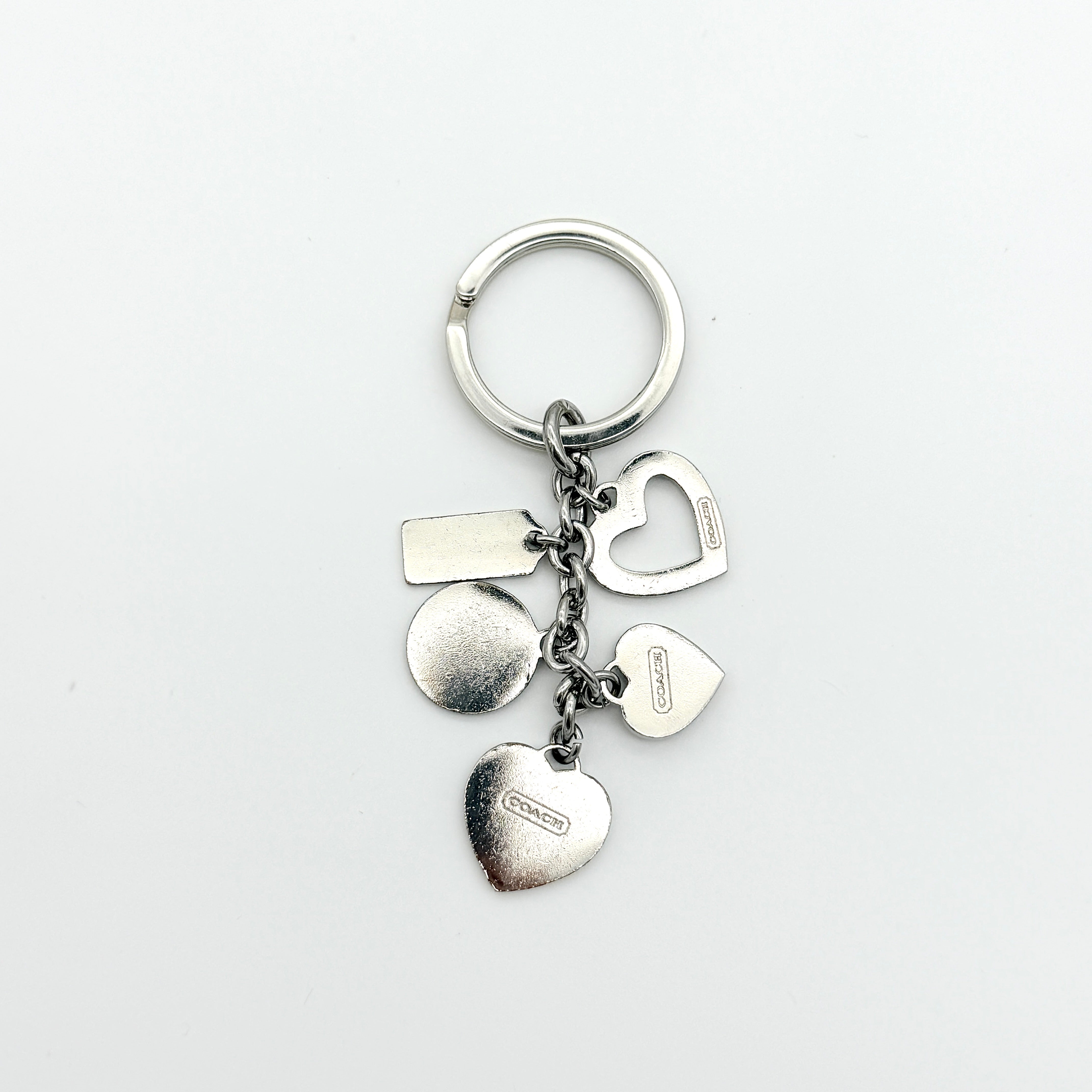 Coach Triple Heart Crystal Charms Keychain in purple and silver-tone, displayed on a Coach-branded drawstring pouch.
