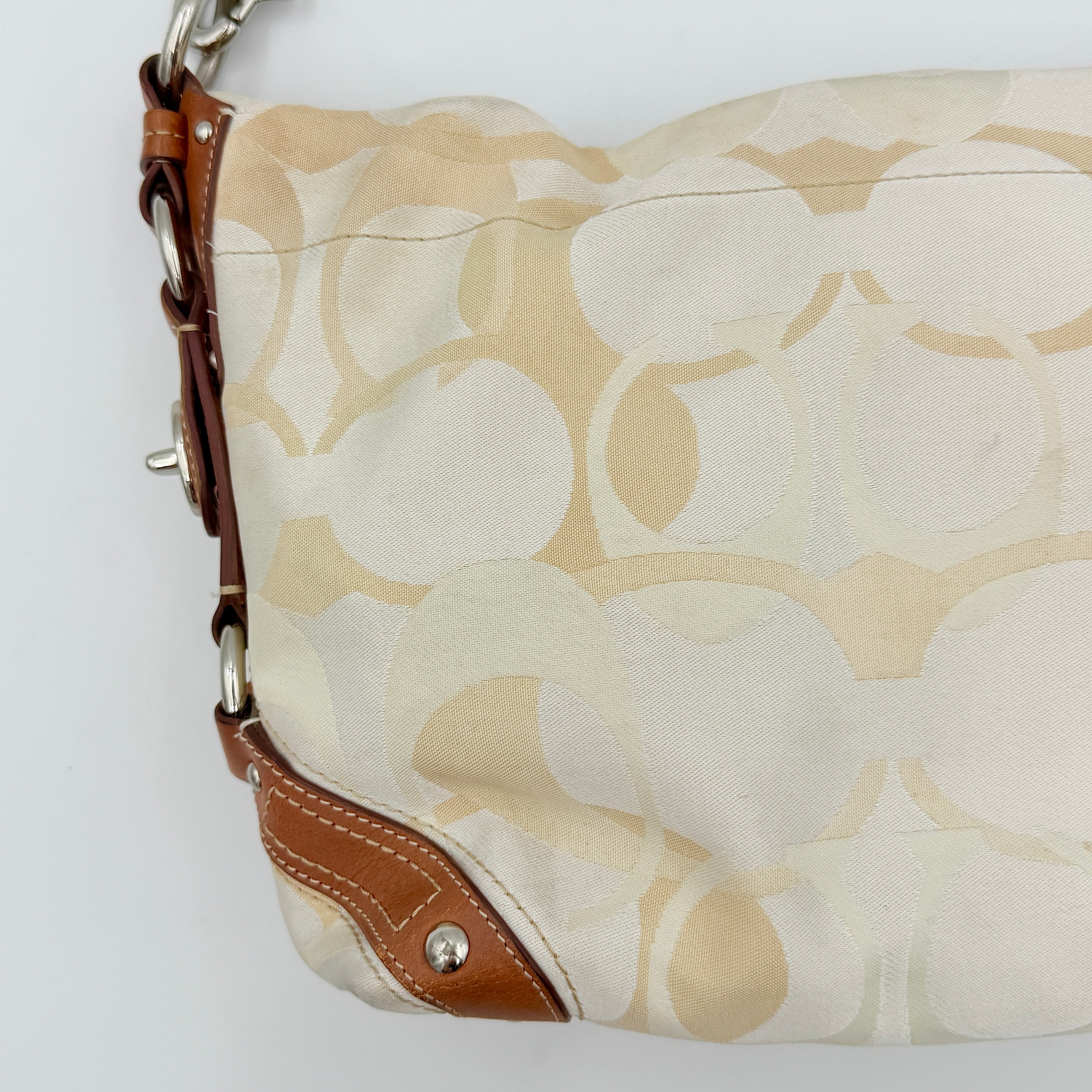 Coach Signature Carly Hobo shoulder bag in cream and brown canvas with tan leather trim and chain-detailed strap.