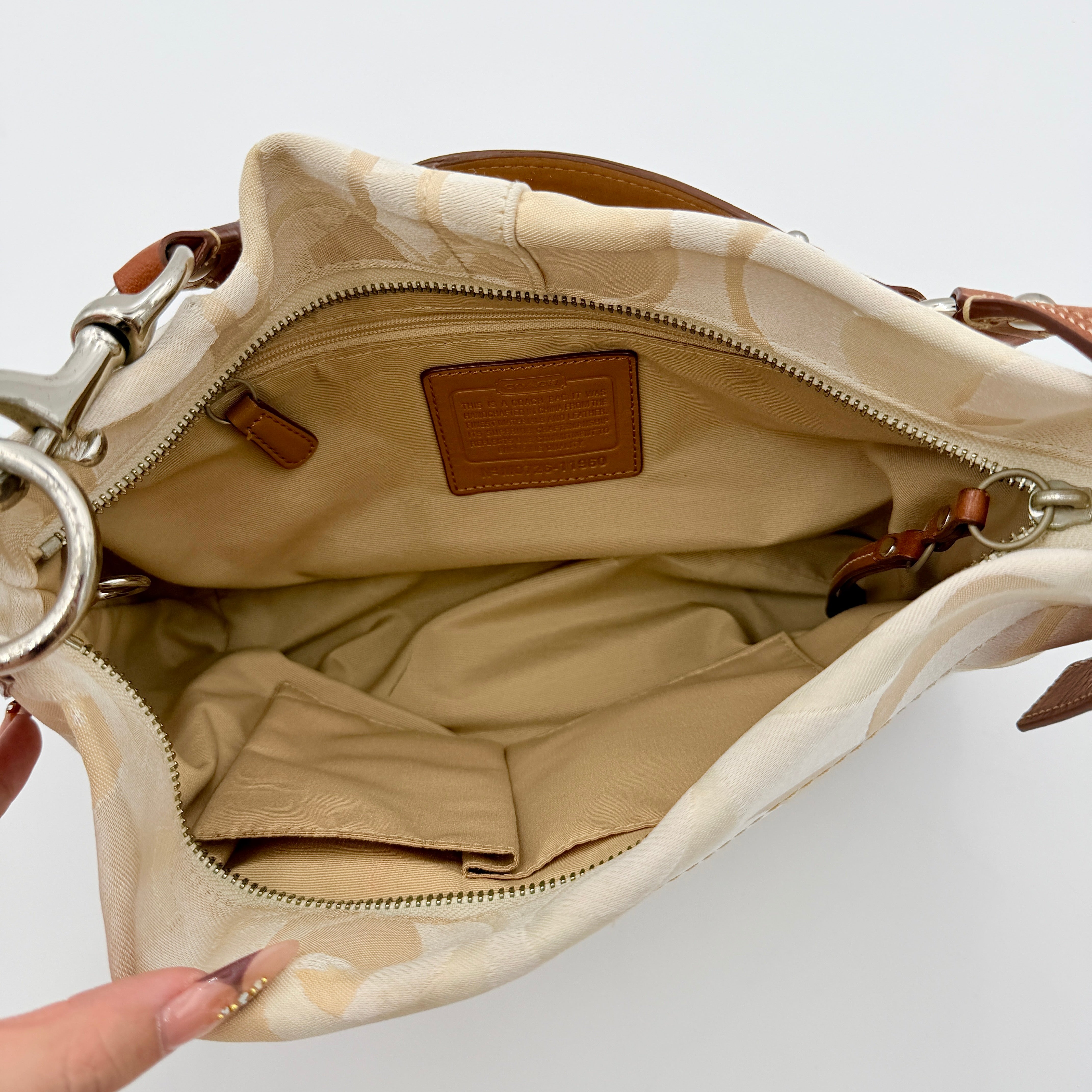 Coach Signature Carly Hobo shoulder bag in cream and brown canvas with tan leather trim and chain-detailed strap.