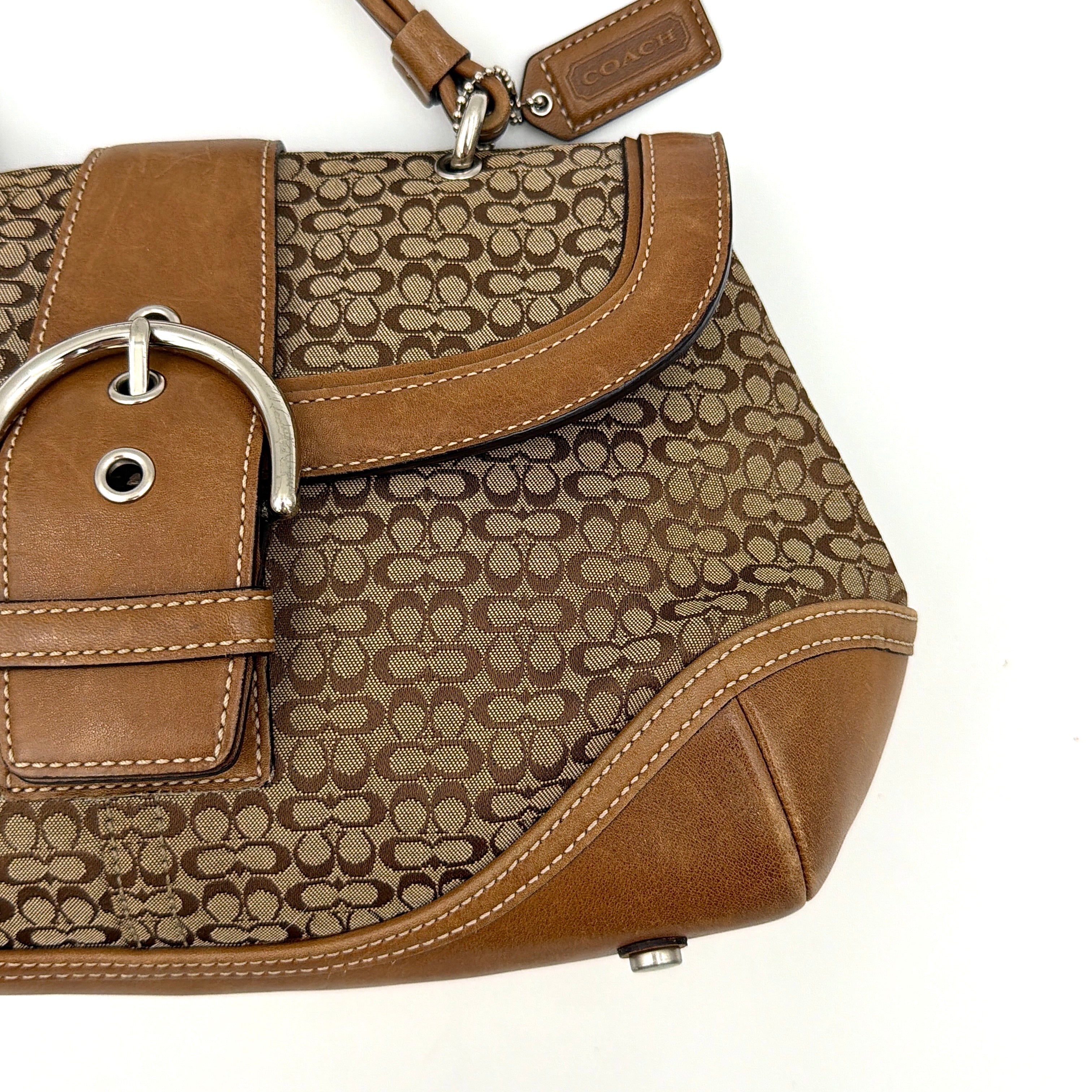 Coach Soho Shoulder Bag in beige and tan monogram jacquard with caramel leather trim, featuring silver hardware and a signature buckle flap.