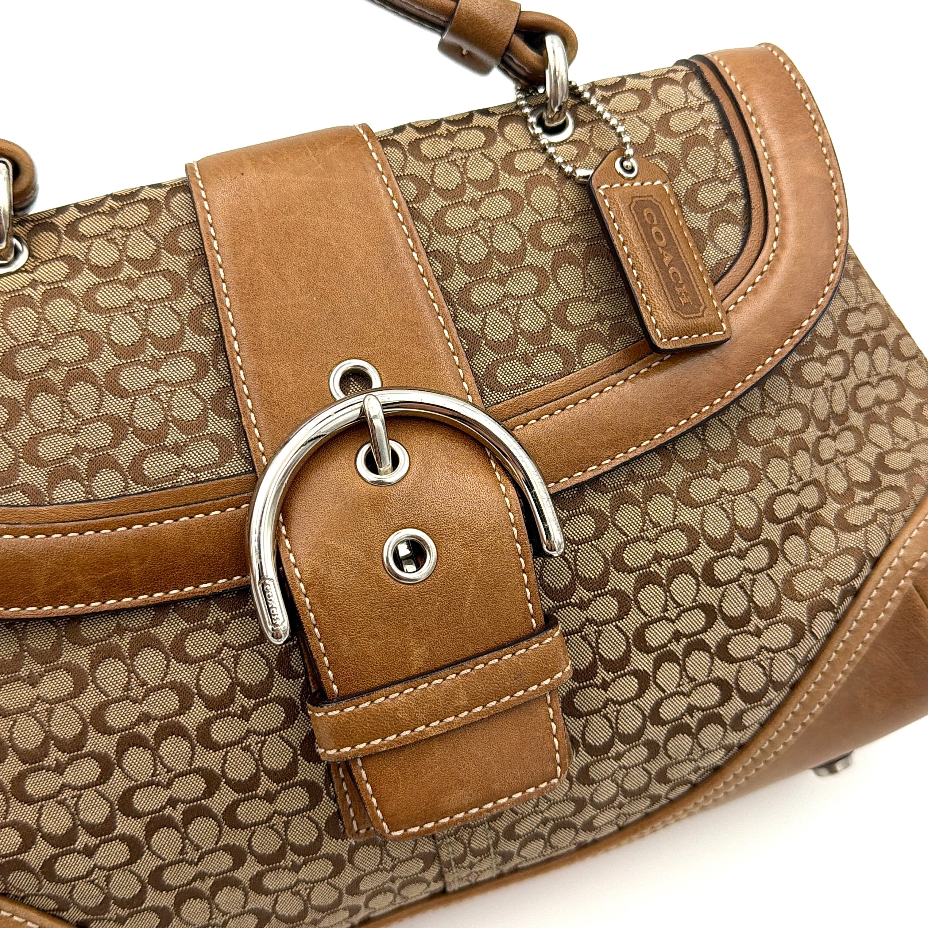 Coach Soho Shoulder Bag in beige and tan monogram jacquard with caramel leather trim, featuring silver hardware and a signature buckle flap.