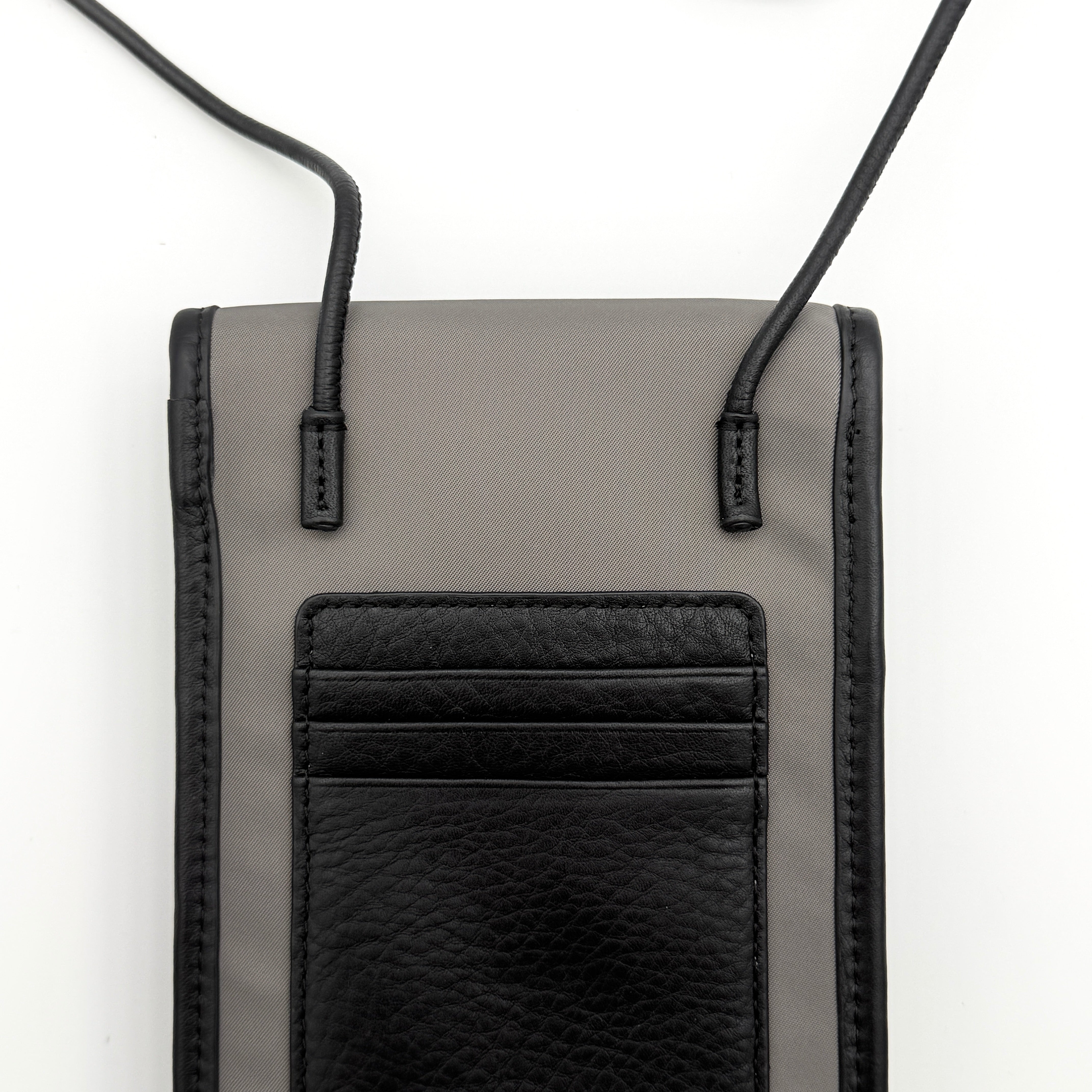 Furla Cosmo grey phone holder with black trim, silver buckle, and black cord strap on white background.