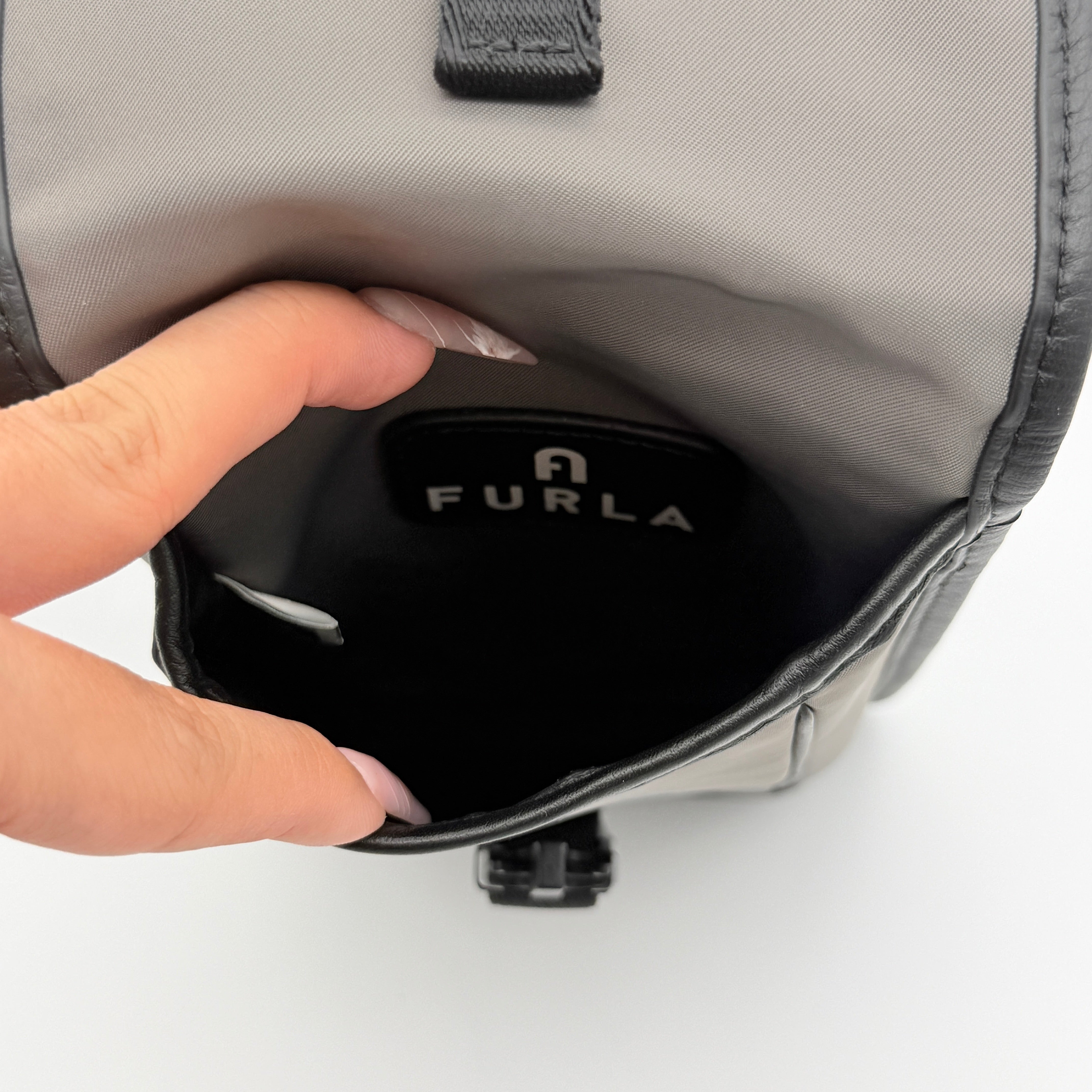 Furla Cosmo grey phone holder with black trim, silver buckle, and black cord strap on white background.
